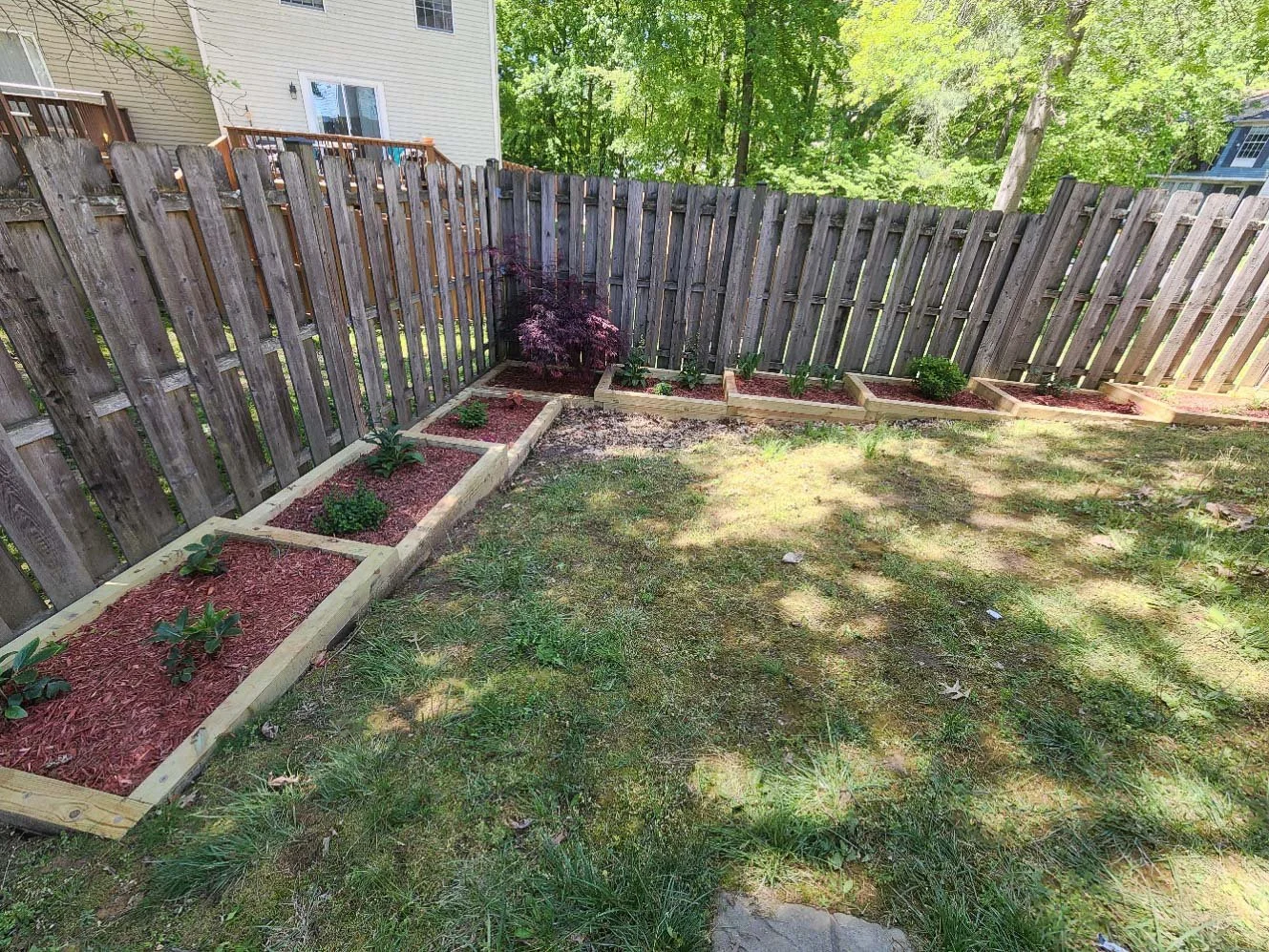 Backyard with a wooden fence, new retaining wall garden beds installed by Severn Excavation and a lawn with trees providing shade.