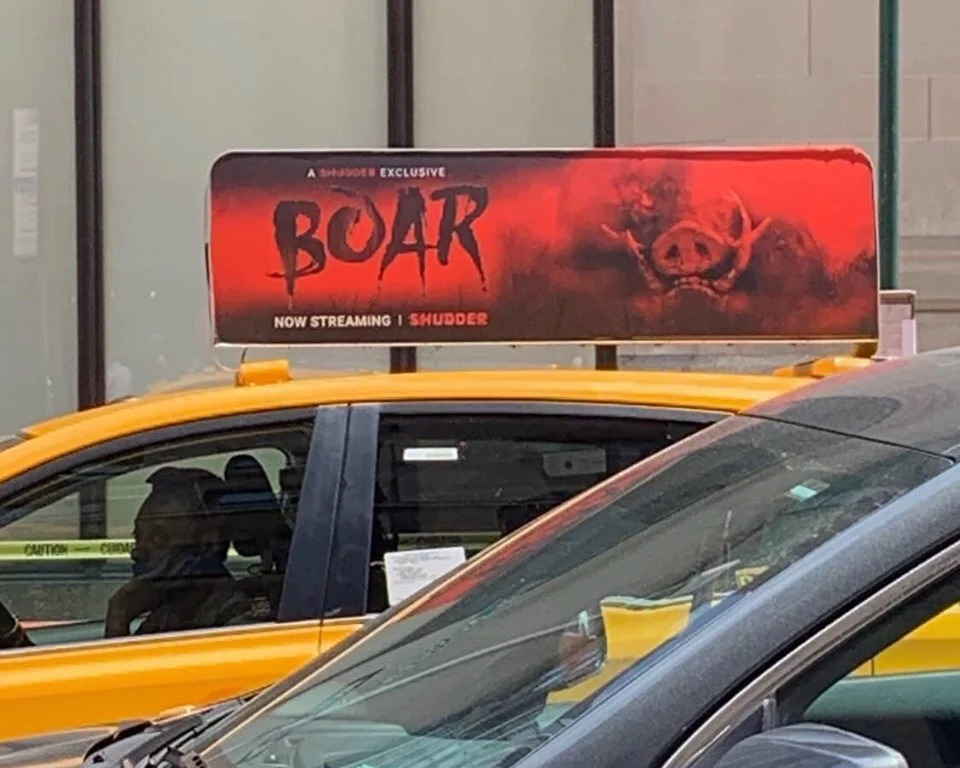A Boar advertisement on top of a yellow New York taxi