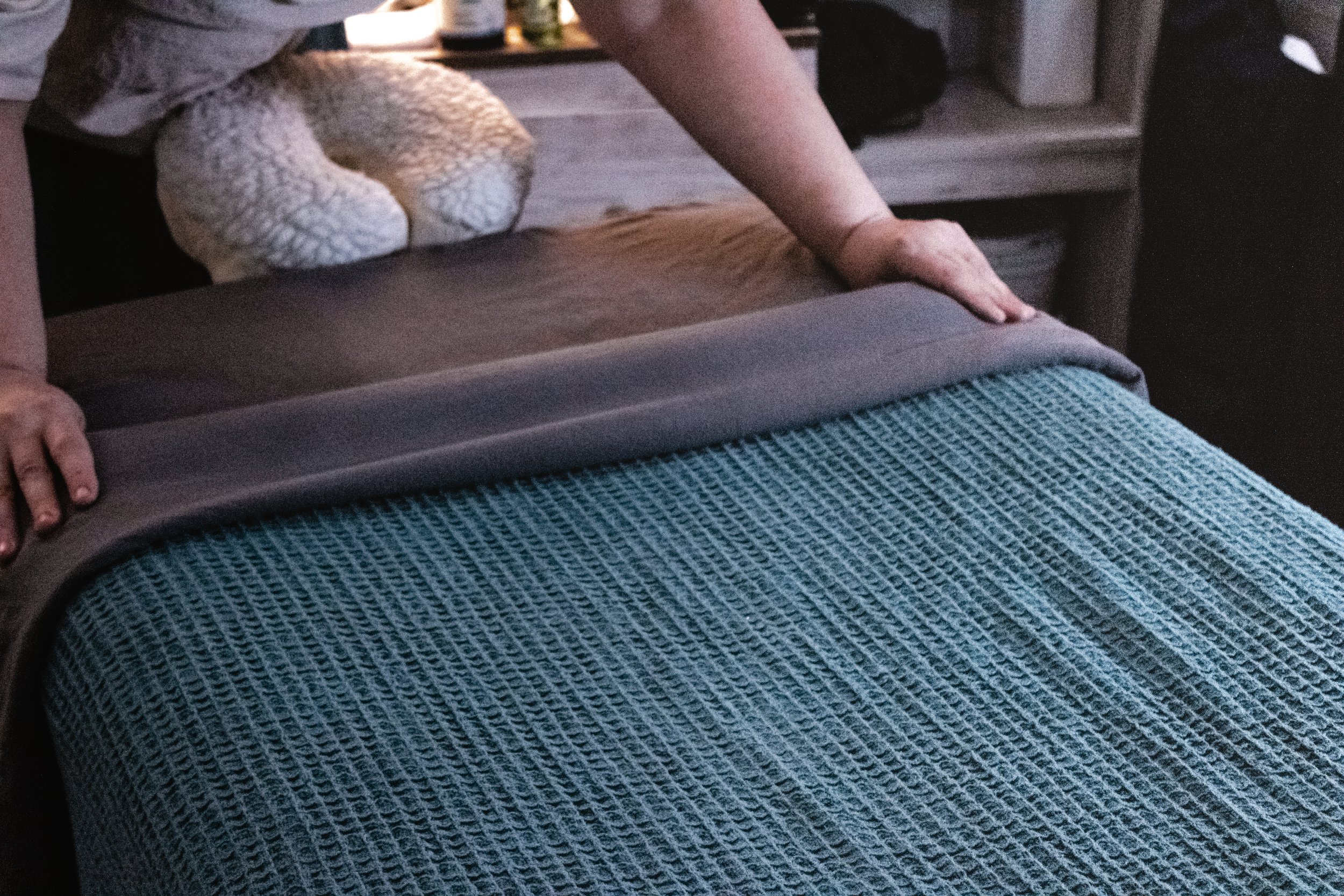 Person smoothing out a bed with a blue textured bedspread in a cozy bedroom.