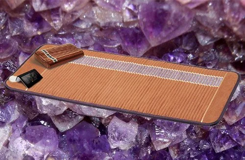 A massage table with a brown cover, a small pillow, and a black box, placed on purple crystalline rocks.