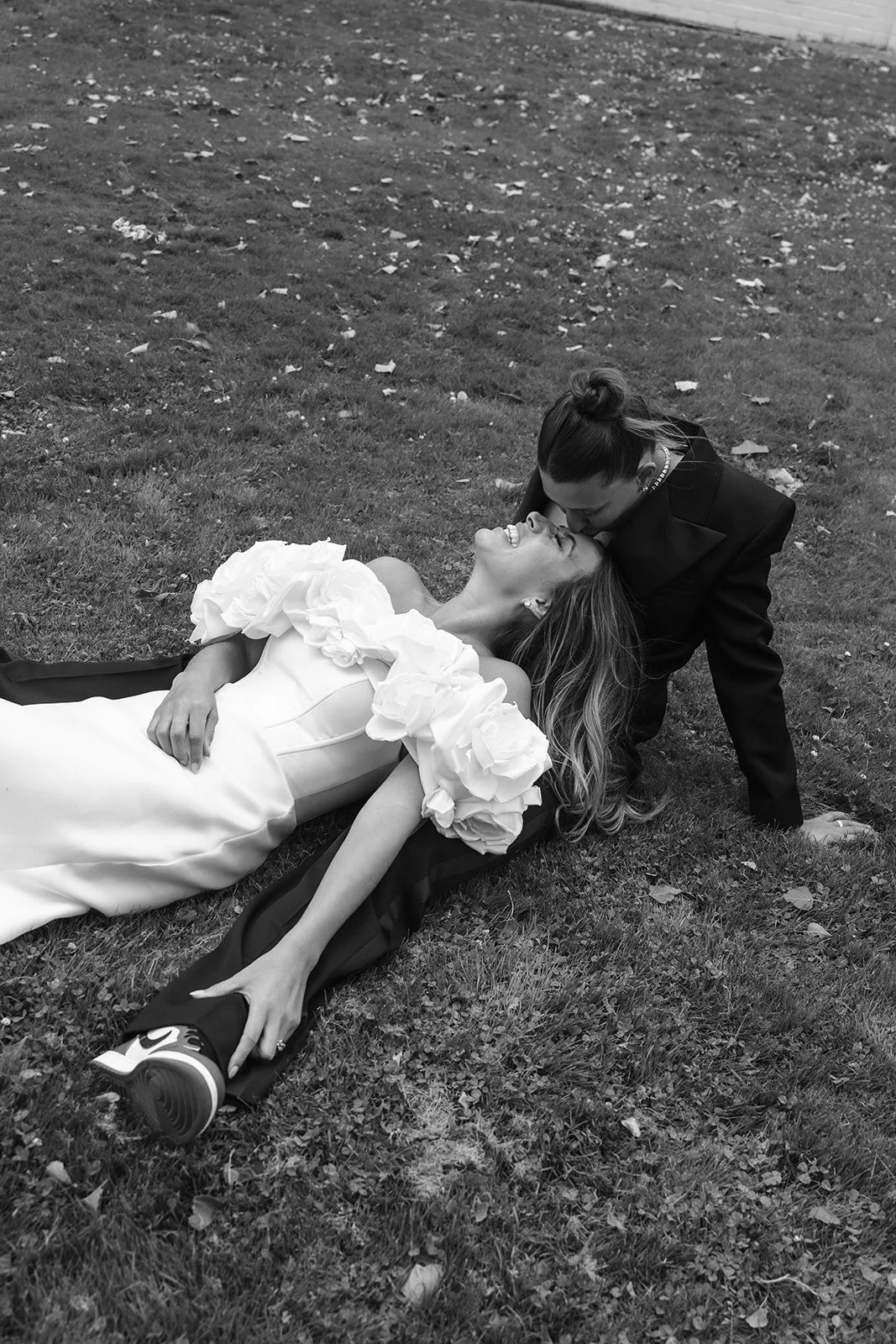 Two brides laying in grass at wedding venue Vaucluse Estate Tasmania with Georgia Burns Wedding Photographer capturing them smiling and kissing each other.