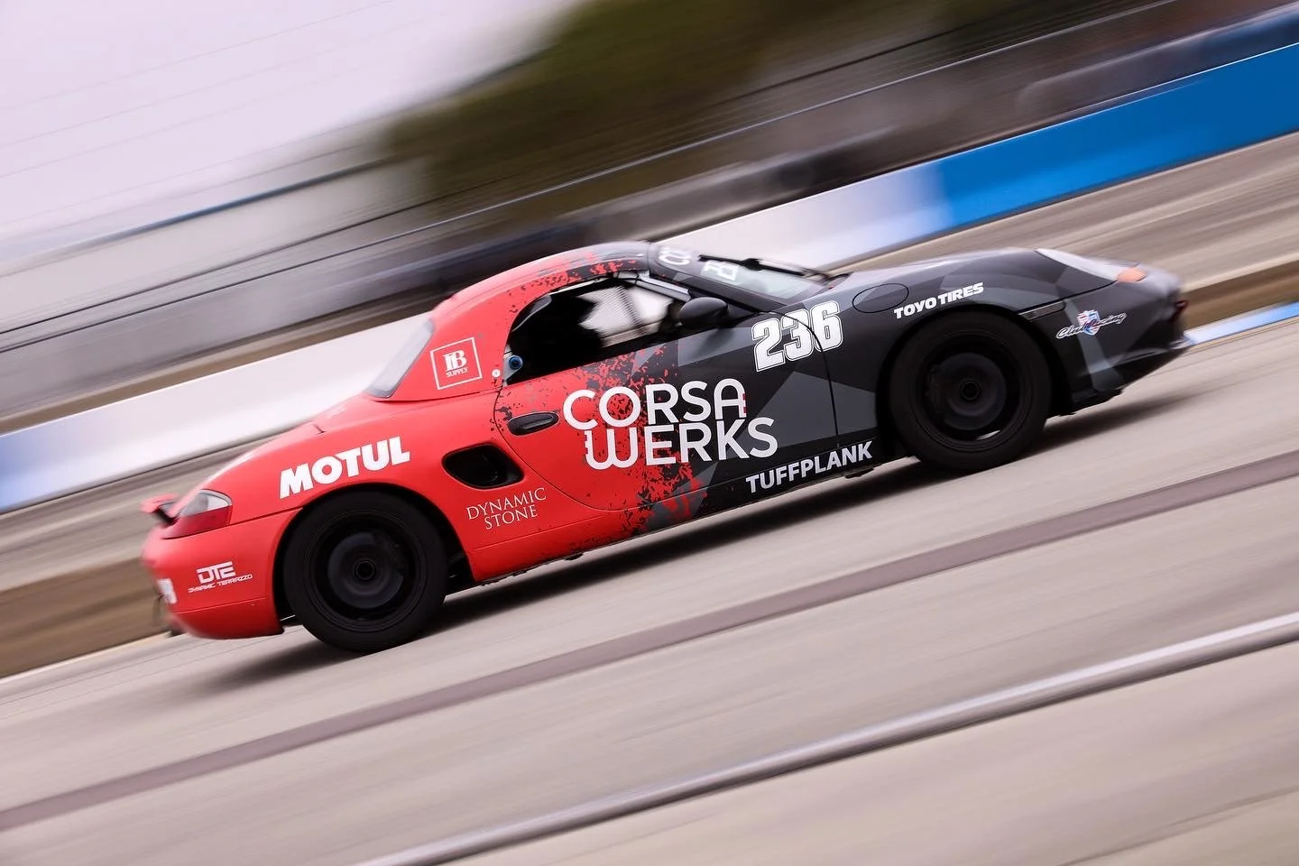 Race car on a track with motion blur, featuring black and red colors and various sponsor logos.