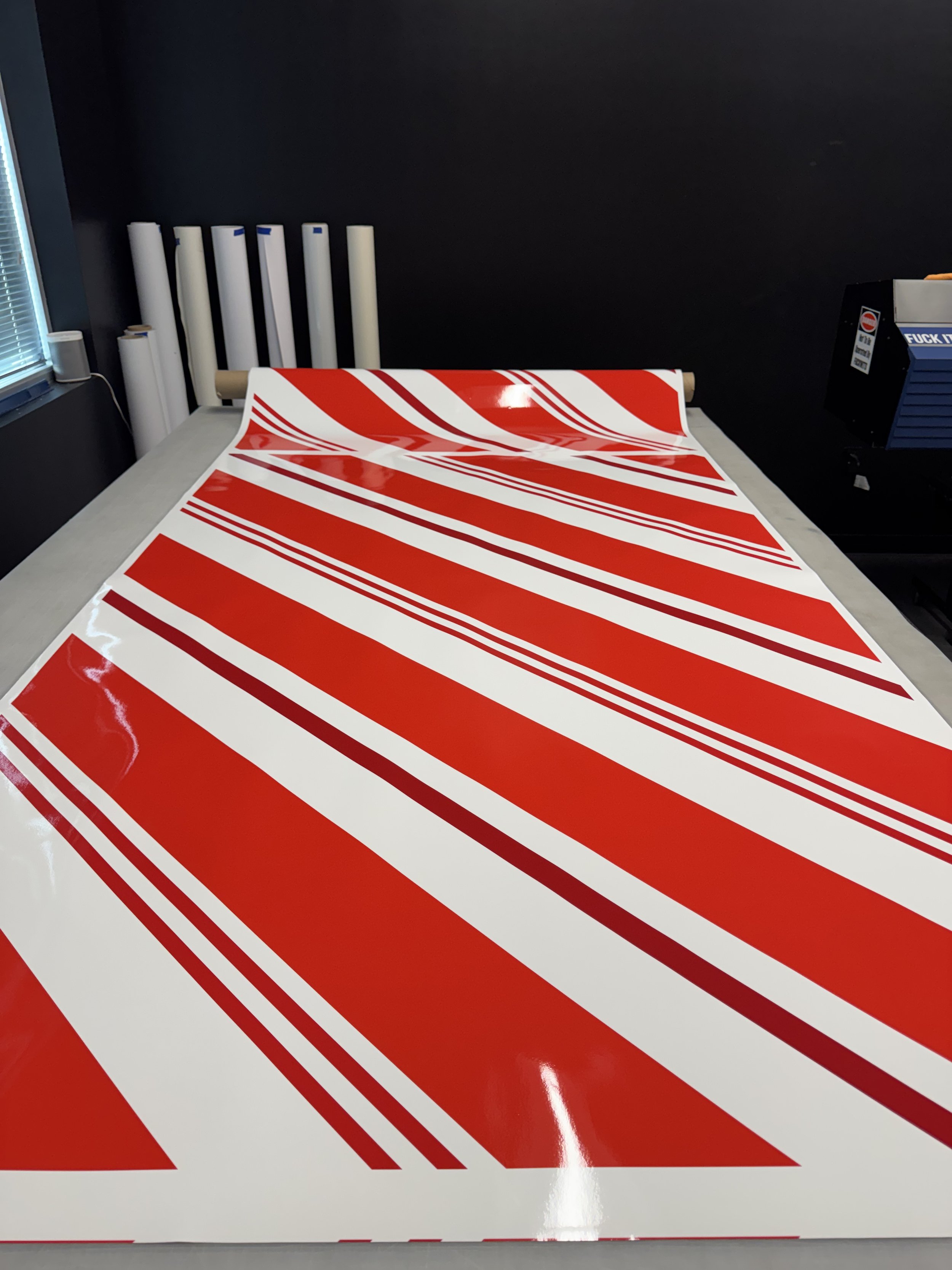 A large sheet of red and white striped decal vinyl on a table, with several rolls of white vinyl in the background.