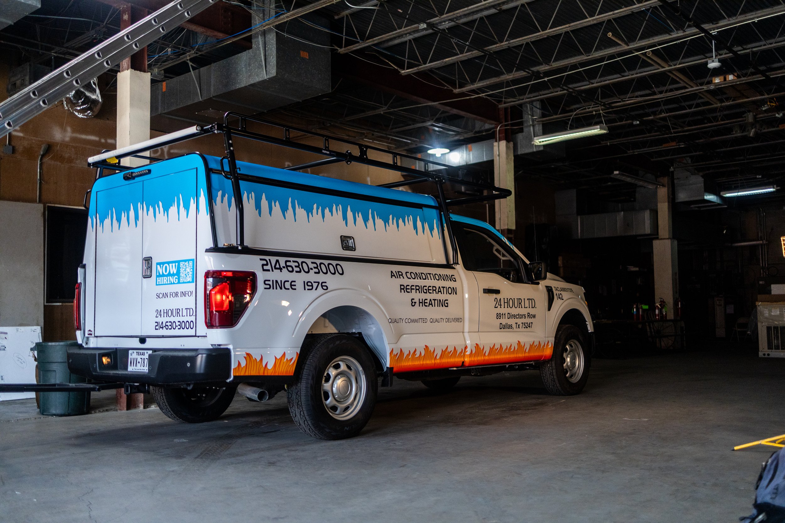 A service van with colorful graphics, advertising air conditioning, refrigeration, and heating services, inside a dimly lit industrial or warehouse space.
