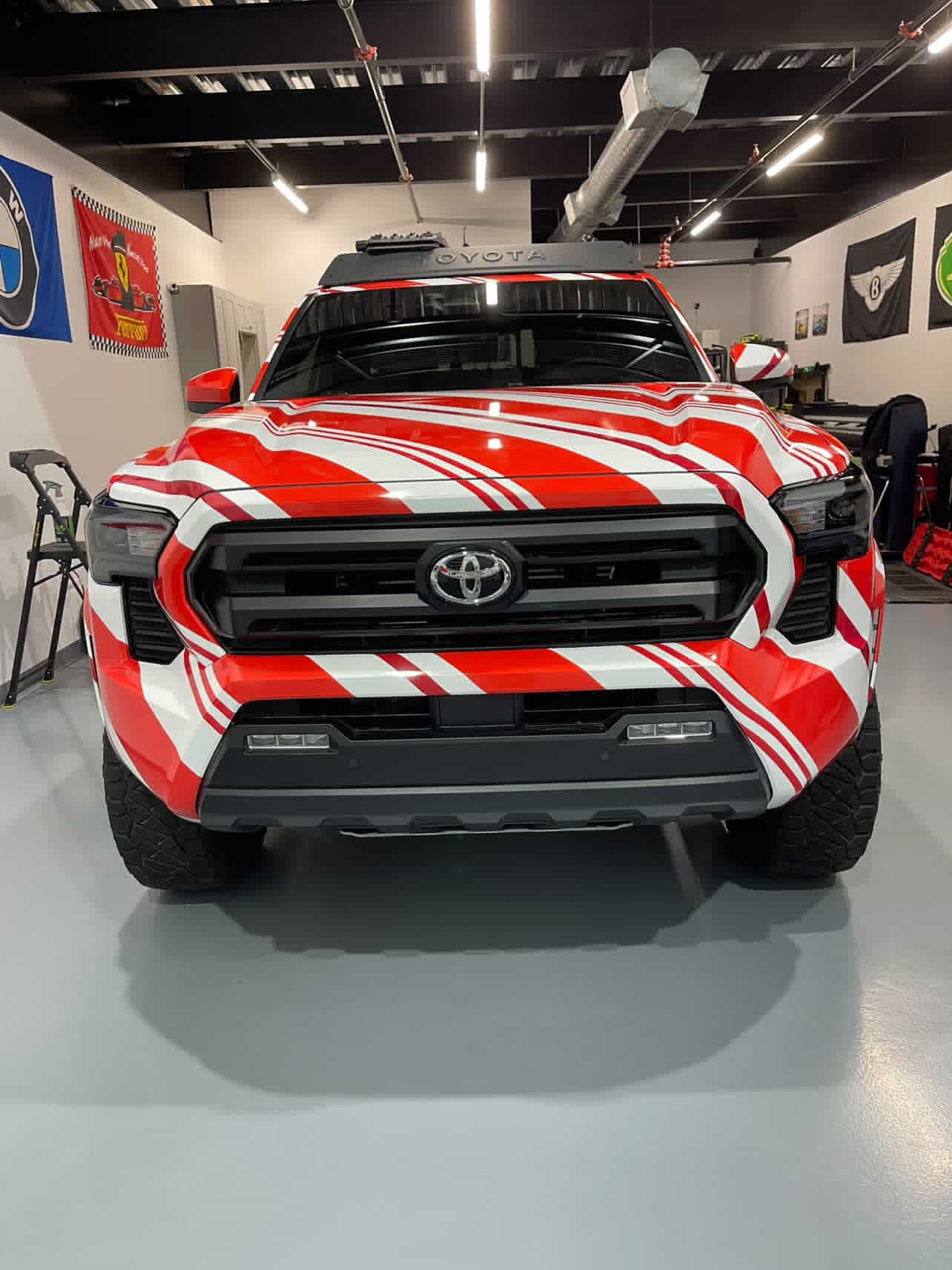 Red and white candy cane Toyota Tacoma pickup truck parked indoors in a garage or showroom.