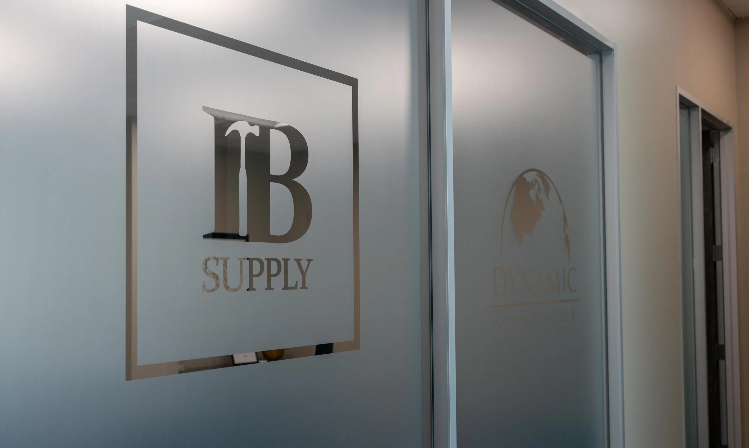 Office glass door with logos, including 'I B SUPPLY' and a globe with 'DYNAMIC' and 'STONE' written below.