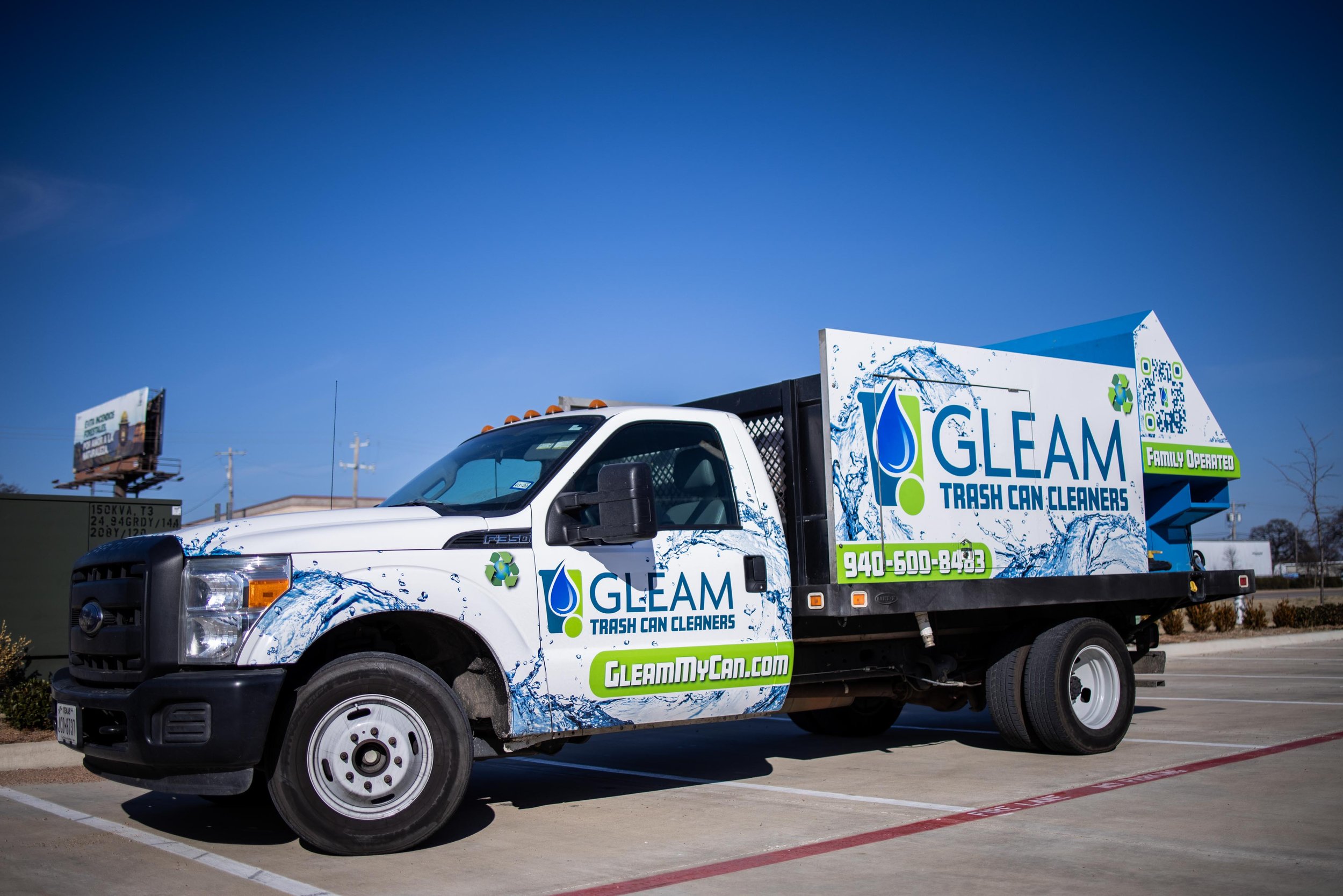 A white truck with blue and green graphics and text advertising Gleam Trash Can Cleaners, parked in a lot under a clear blue sky.