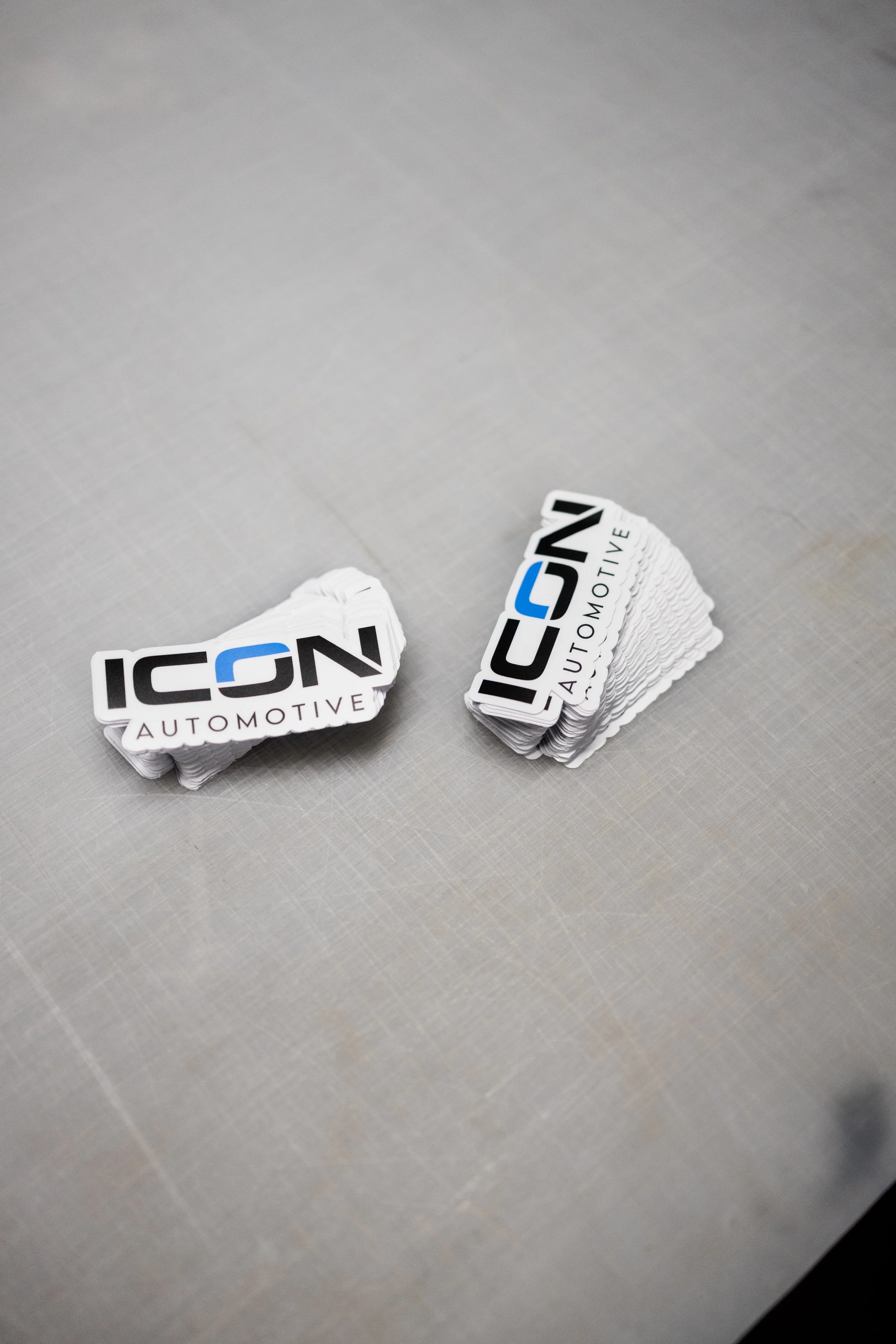 Two stacks of ICON Automotive stickers on a light-colored textured surface.