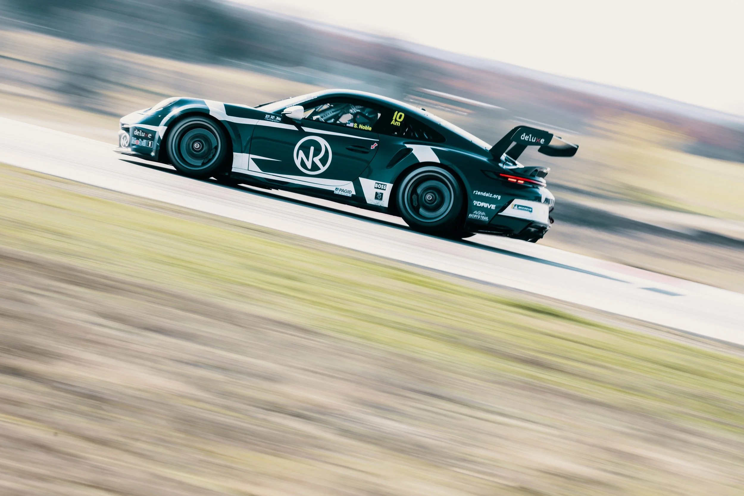 A black racing car with a large rear wing moving at high speed on a race track.
