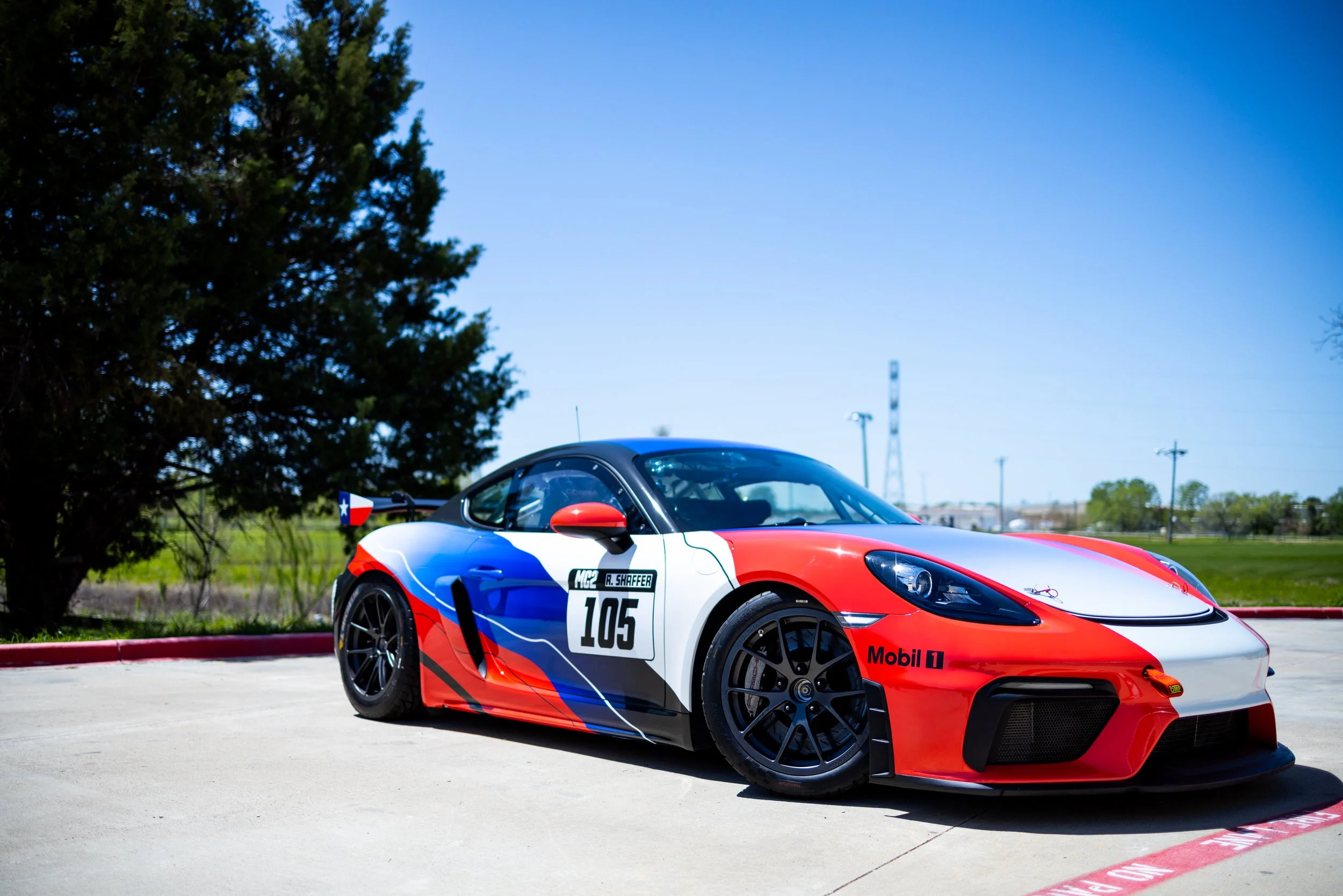 A race car with a red, white, and blue paint scheme parked outdoors on a sunny day.