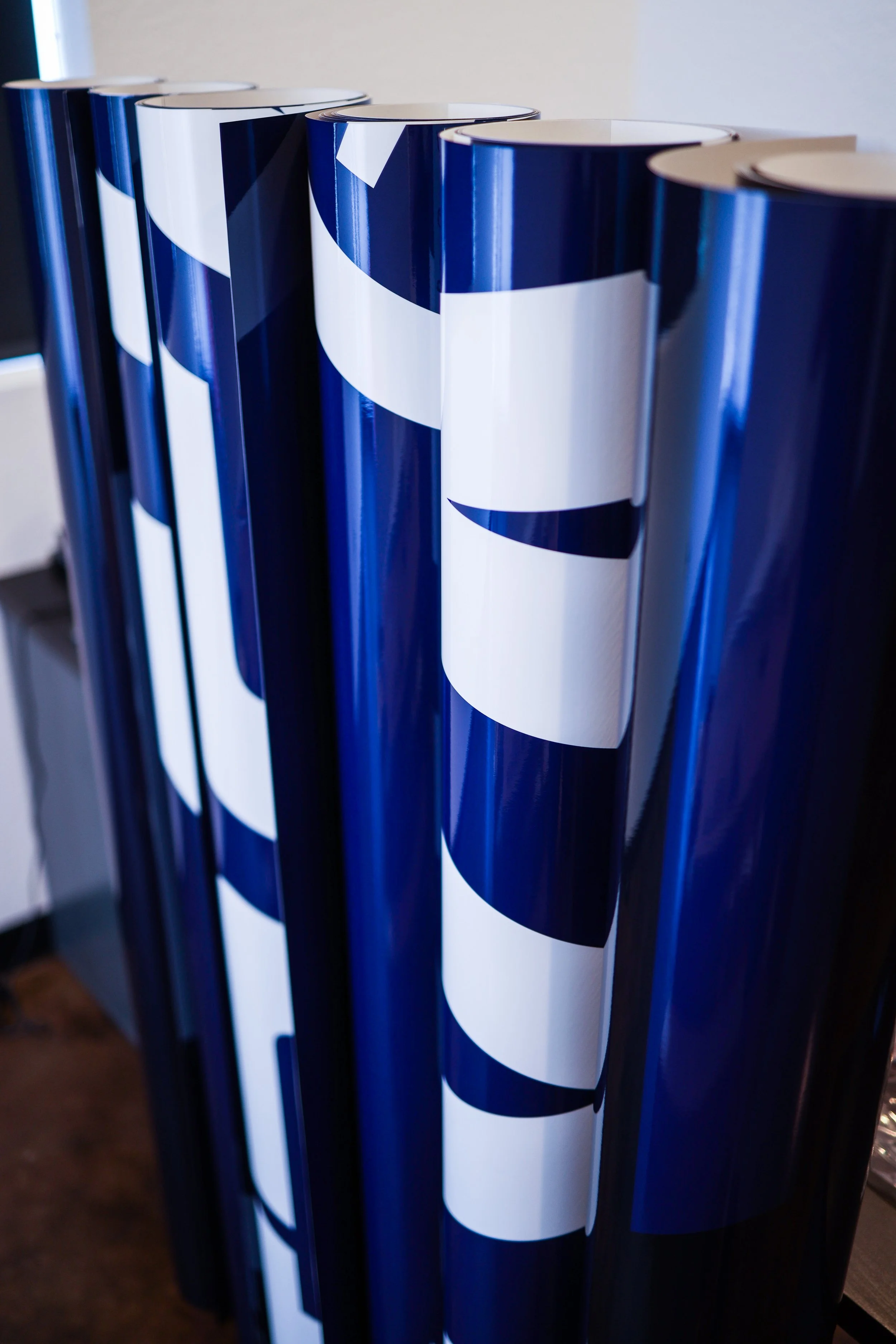 Blue cylindrical objects with white and dark blue patterns, likely wrapping paper or posters, stacked vertically on a surface.
