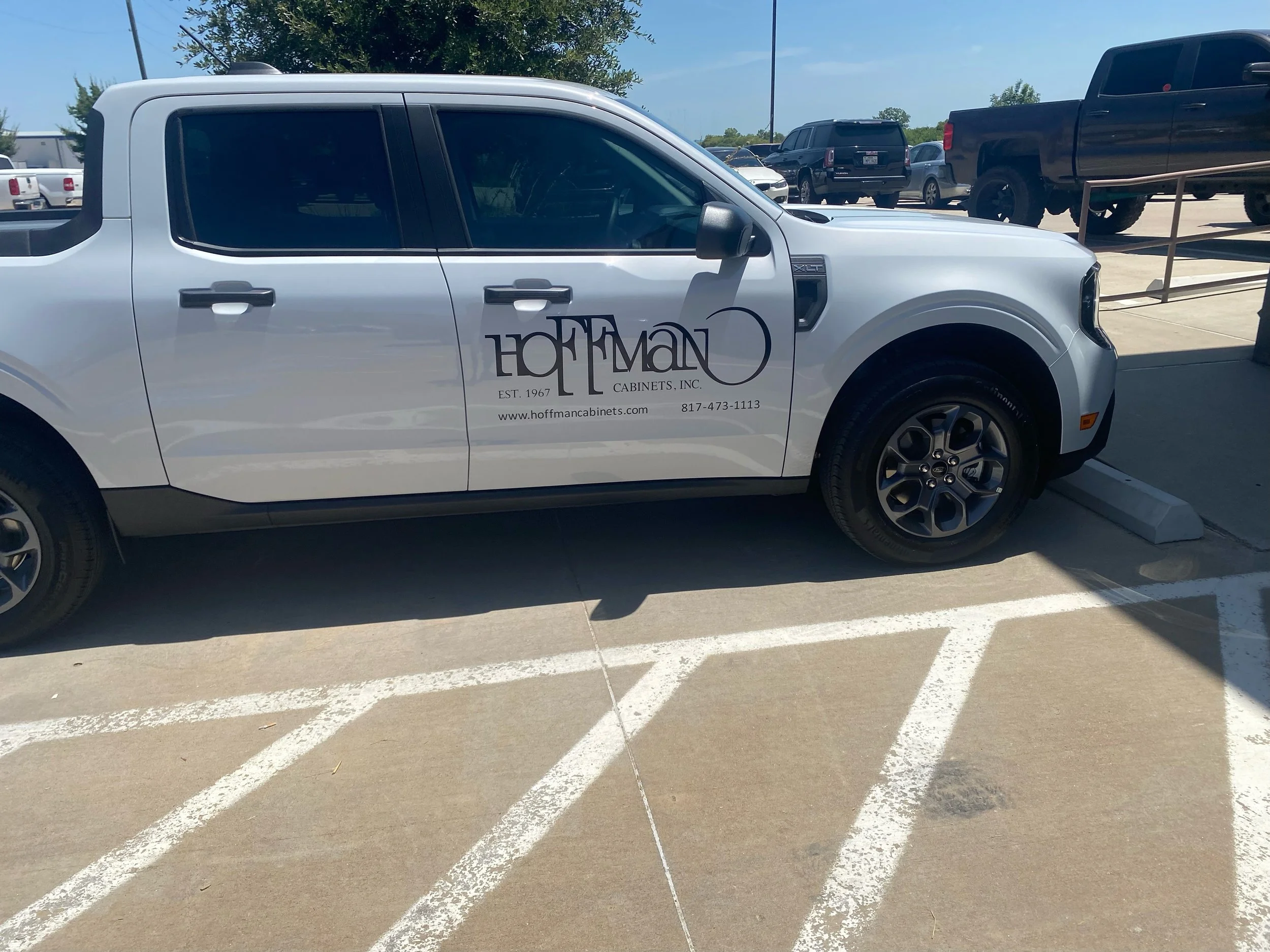 White pickup truck parked in a striped parking space, advertising Hoffman Cabinets Inc. with contact information and logo on the side.