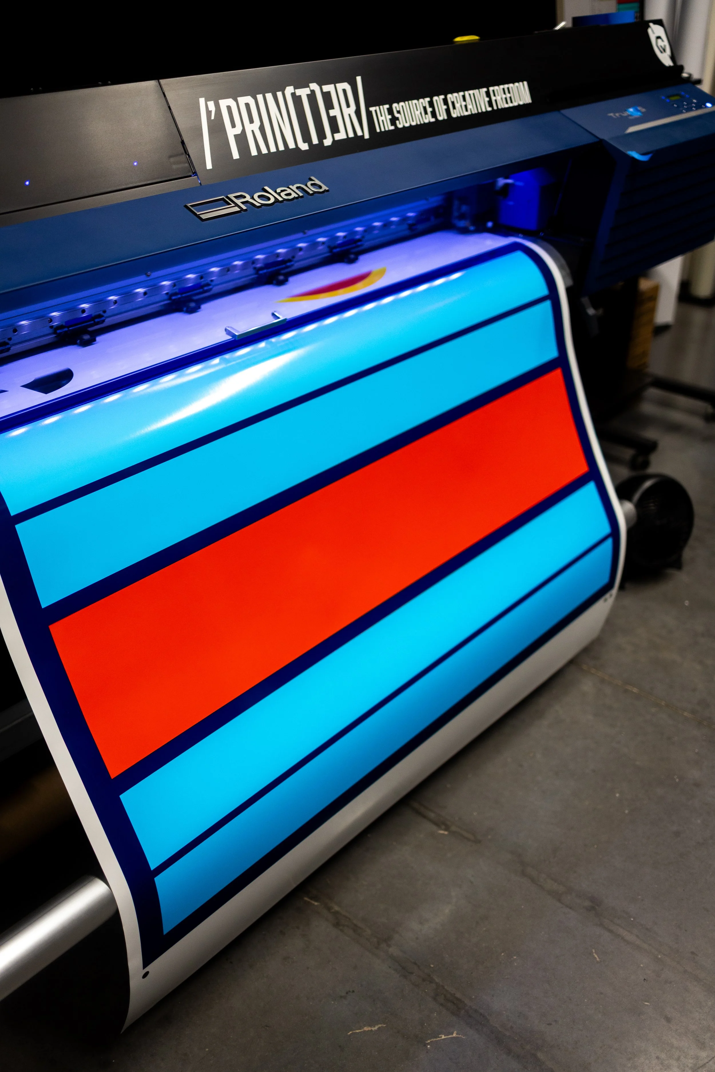 Roland large-format printer printing a colorful image with blue and orange stripes.