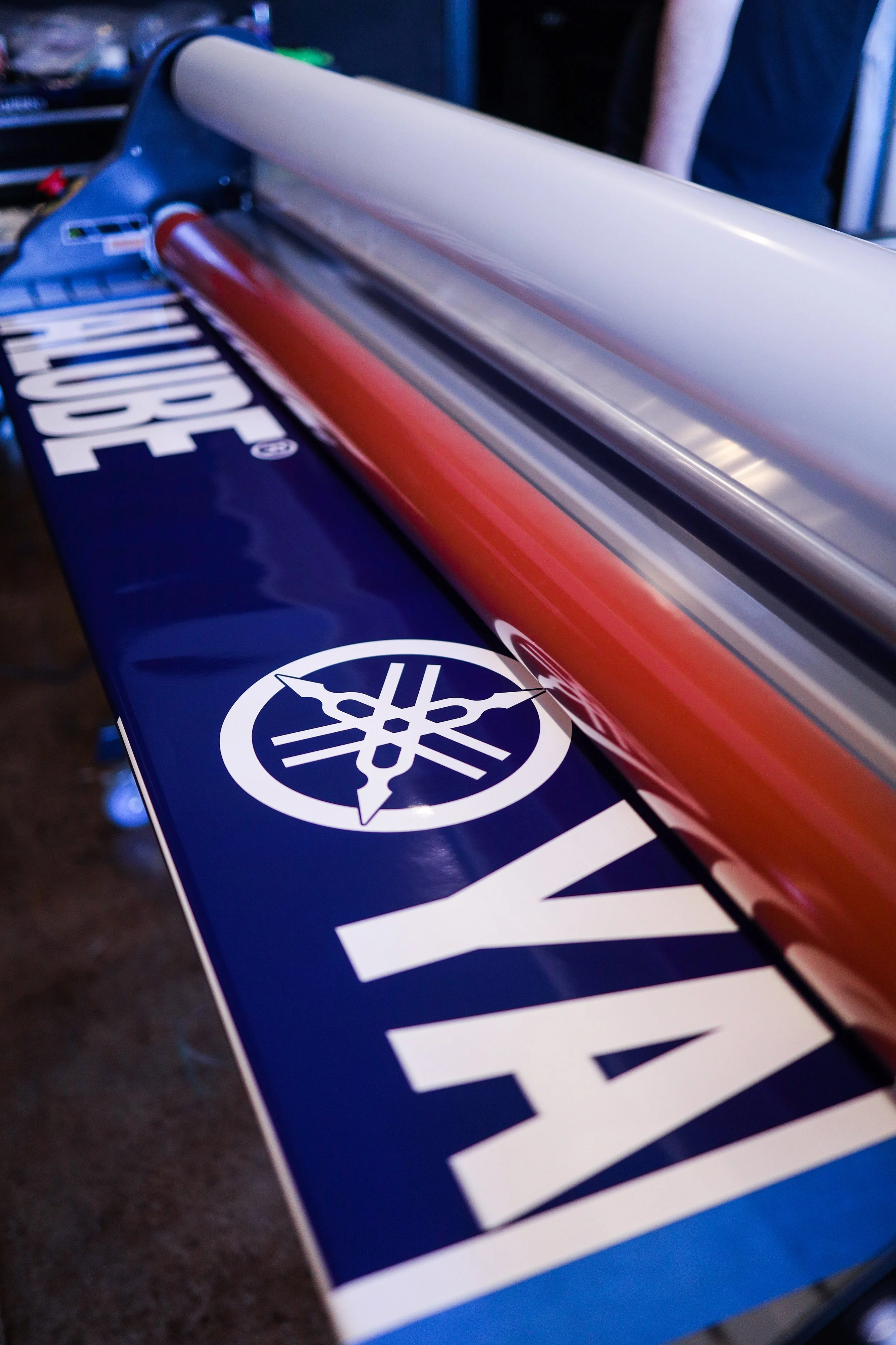Close-up of a Yamaha motorcycle logo and text on a blue surface with a reflective red and white cylindrical object laying on top.