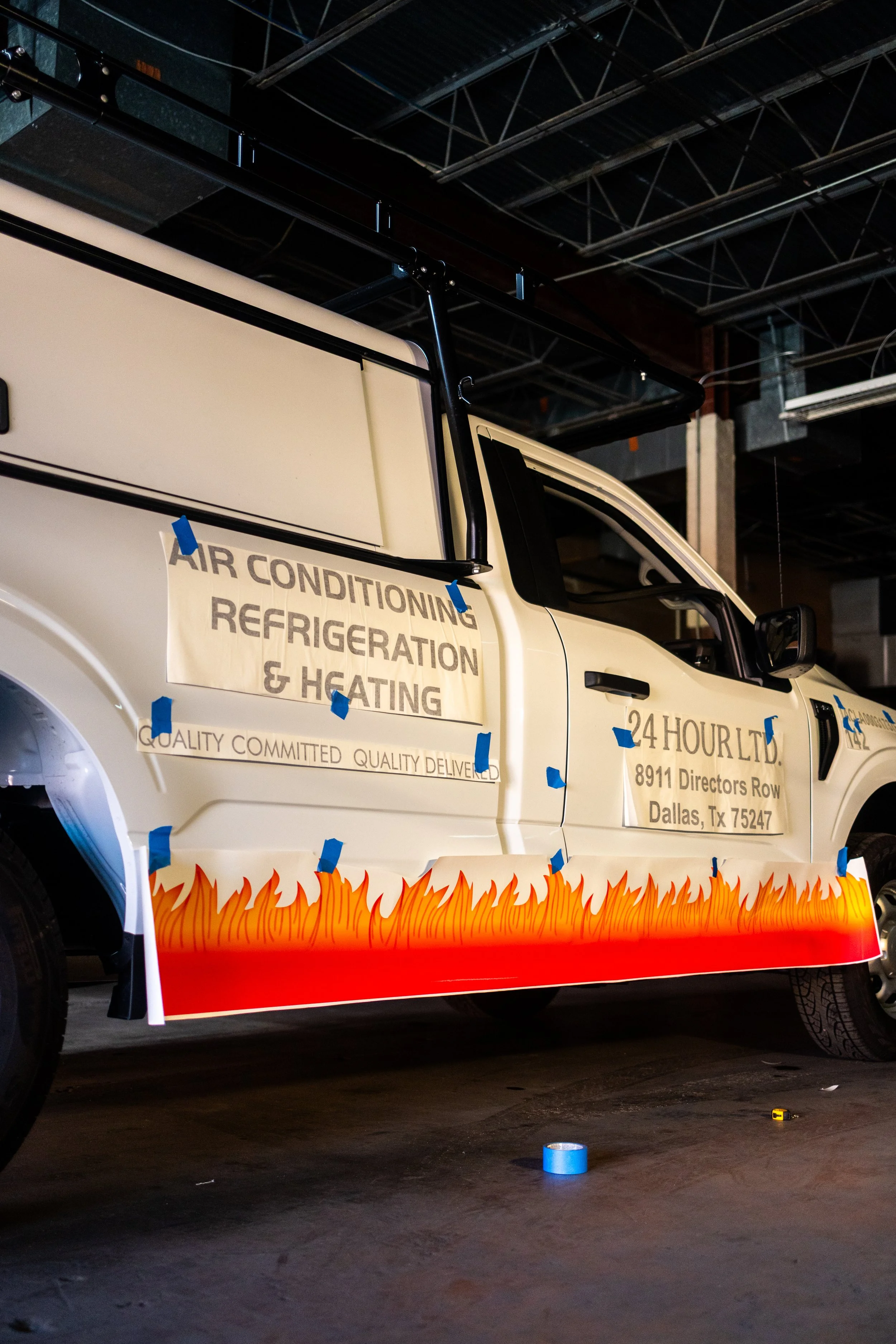 A truck with signage advertising air conditioning, refrigeration, and heating services in Dallas, Texas, parked indoors in a warehouse.