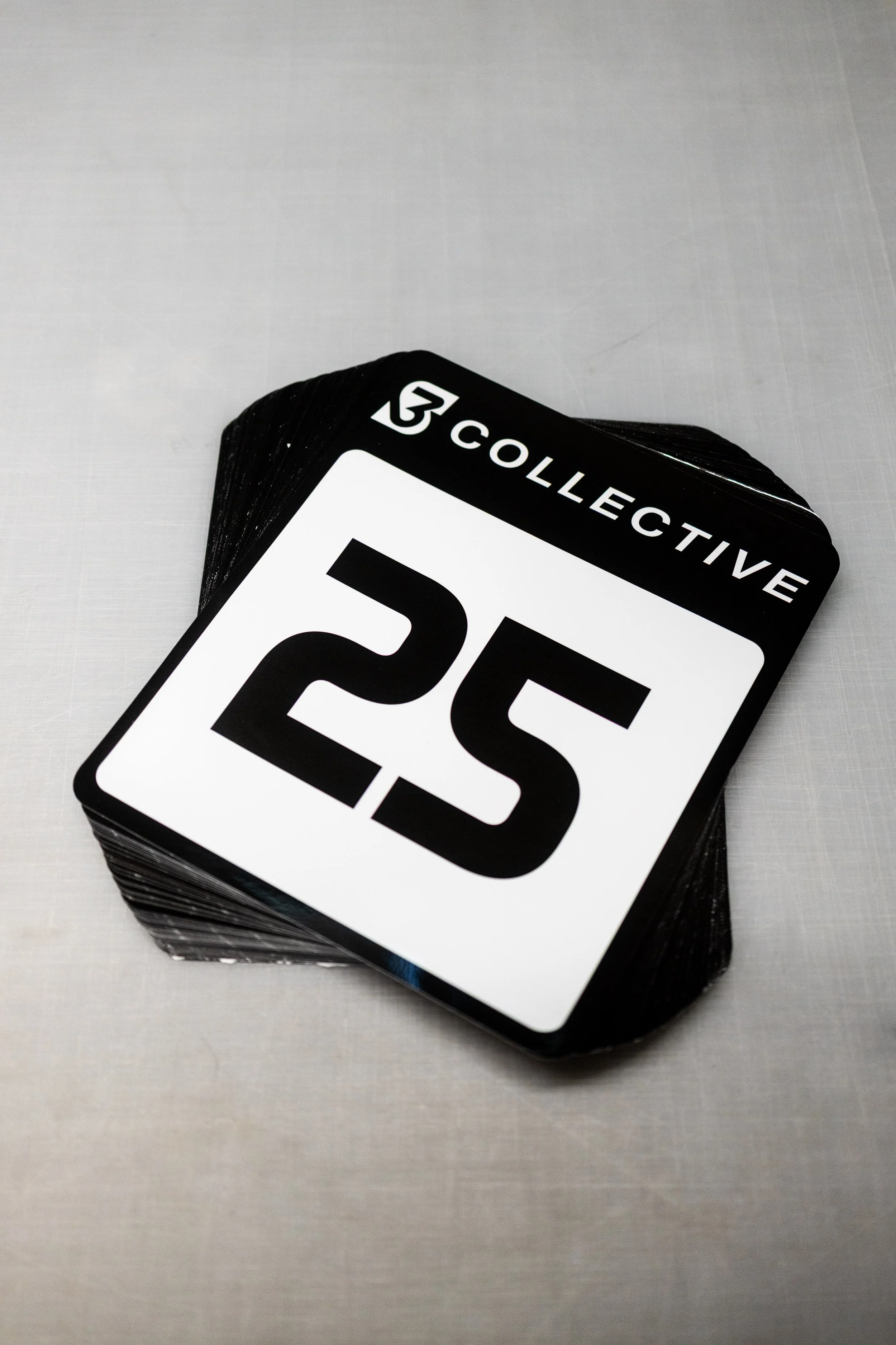 Stack of black and white cards with the number 25 and the text 'COLLECTIVE' on top, placed on a light gray surface.
