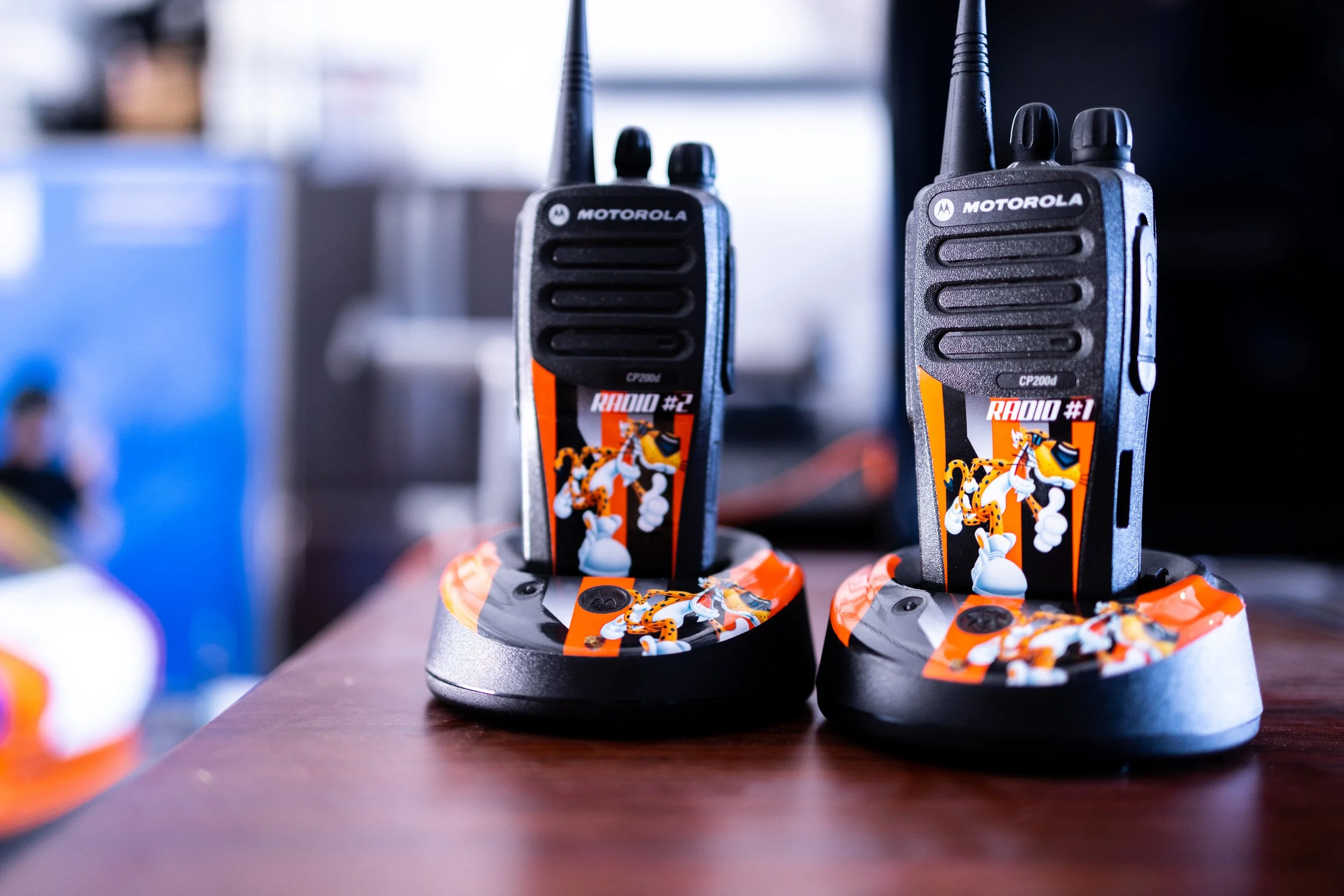 Two walkie-talkies are positioned on charging docks on a wooden surface. The walkie-talkies are decorated with a cartoon character, Tigger from Winnie the Pooh, and the words 'RADIO #1' and 'RADIO #2'.
