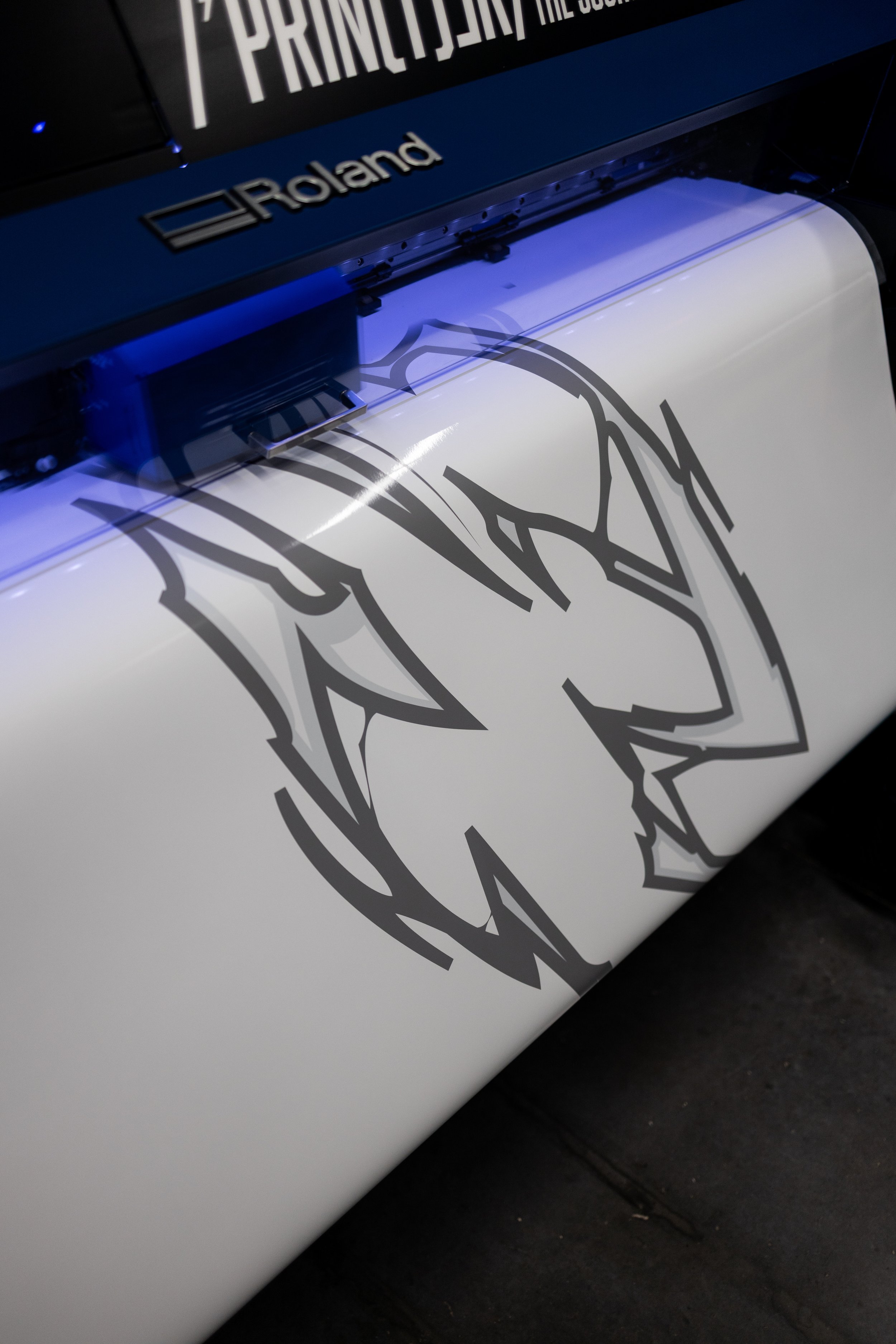 Close-up of a vinyl printing machine applying a black tribal-style design onto a white surface.
