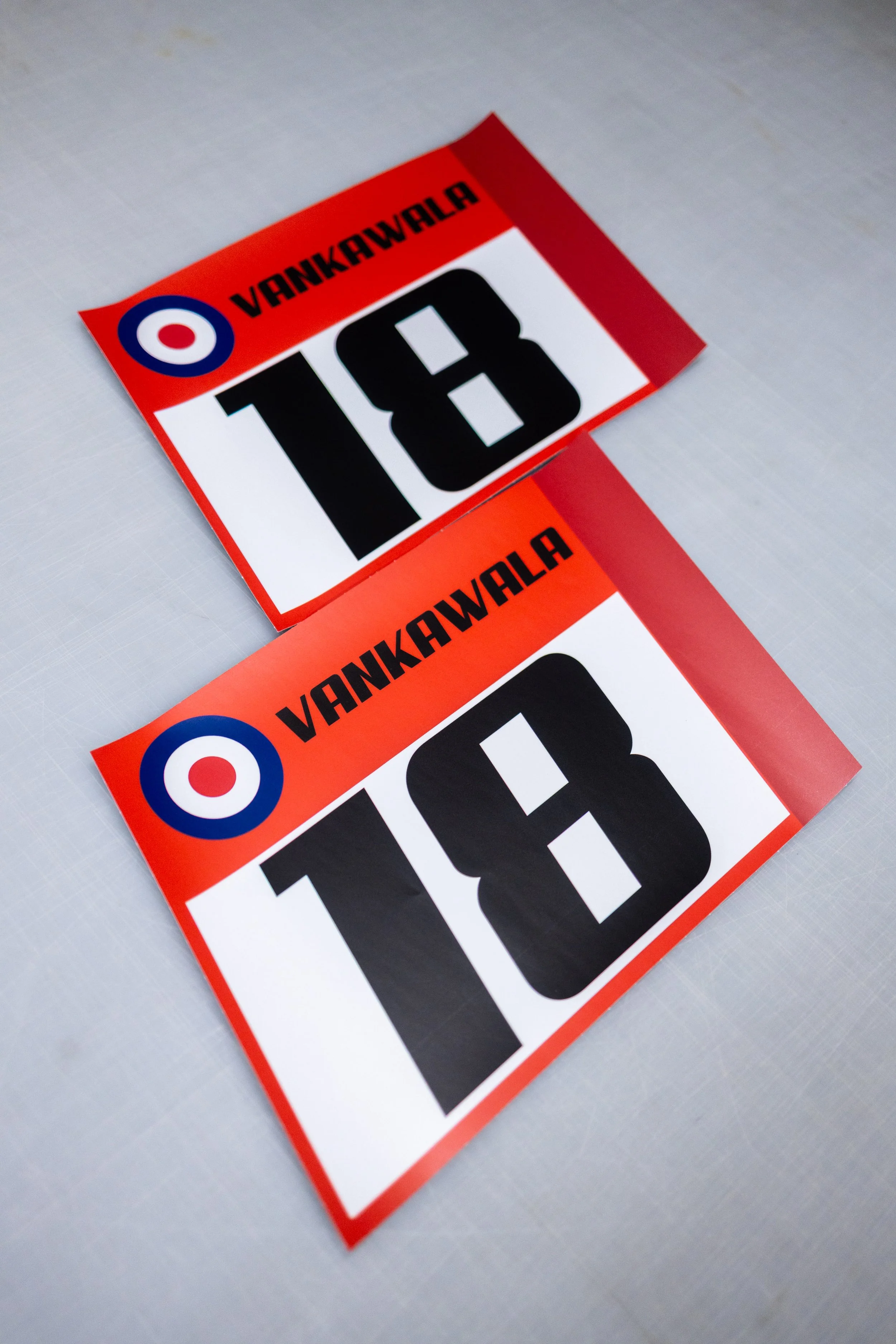 Two racing bibs with the number 18 and the name Vankawala, on a light-colored surface.