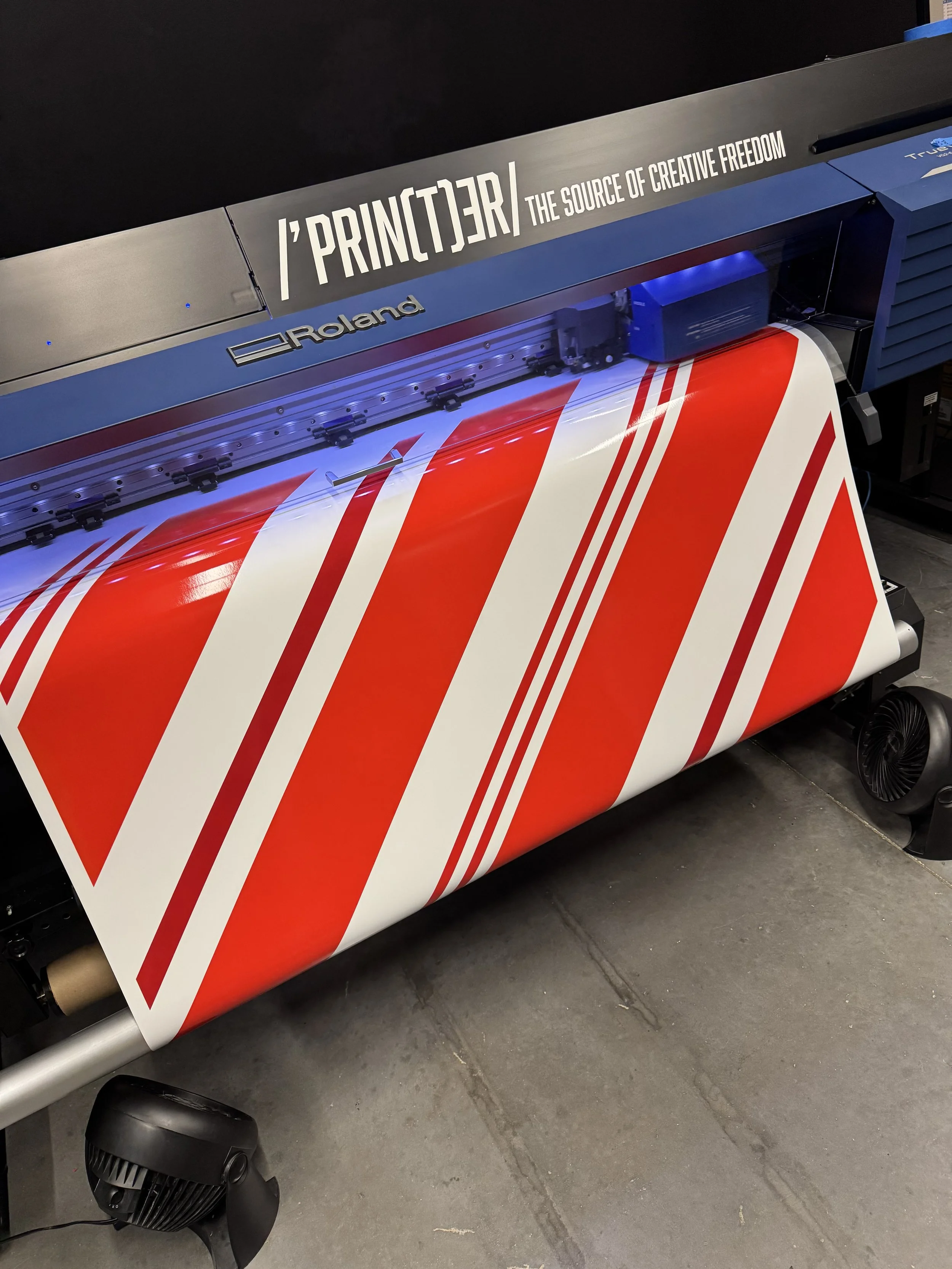 A large Roland printer printing a red and white striped pattern on a roll of material.