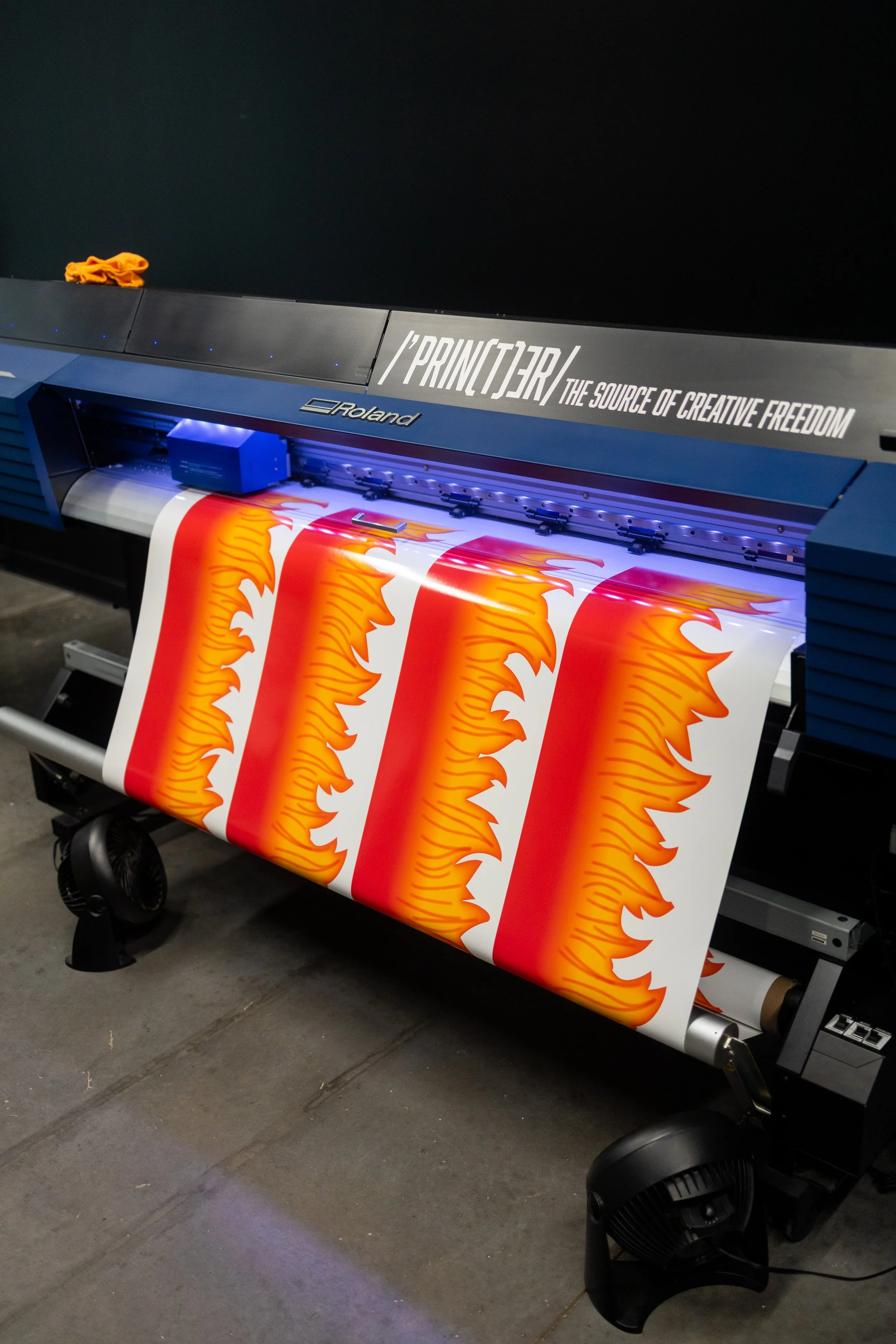 Large format printer printing a vibrant orange and red flame graphic on a white banner.