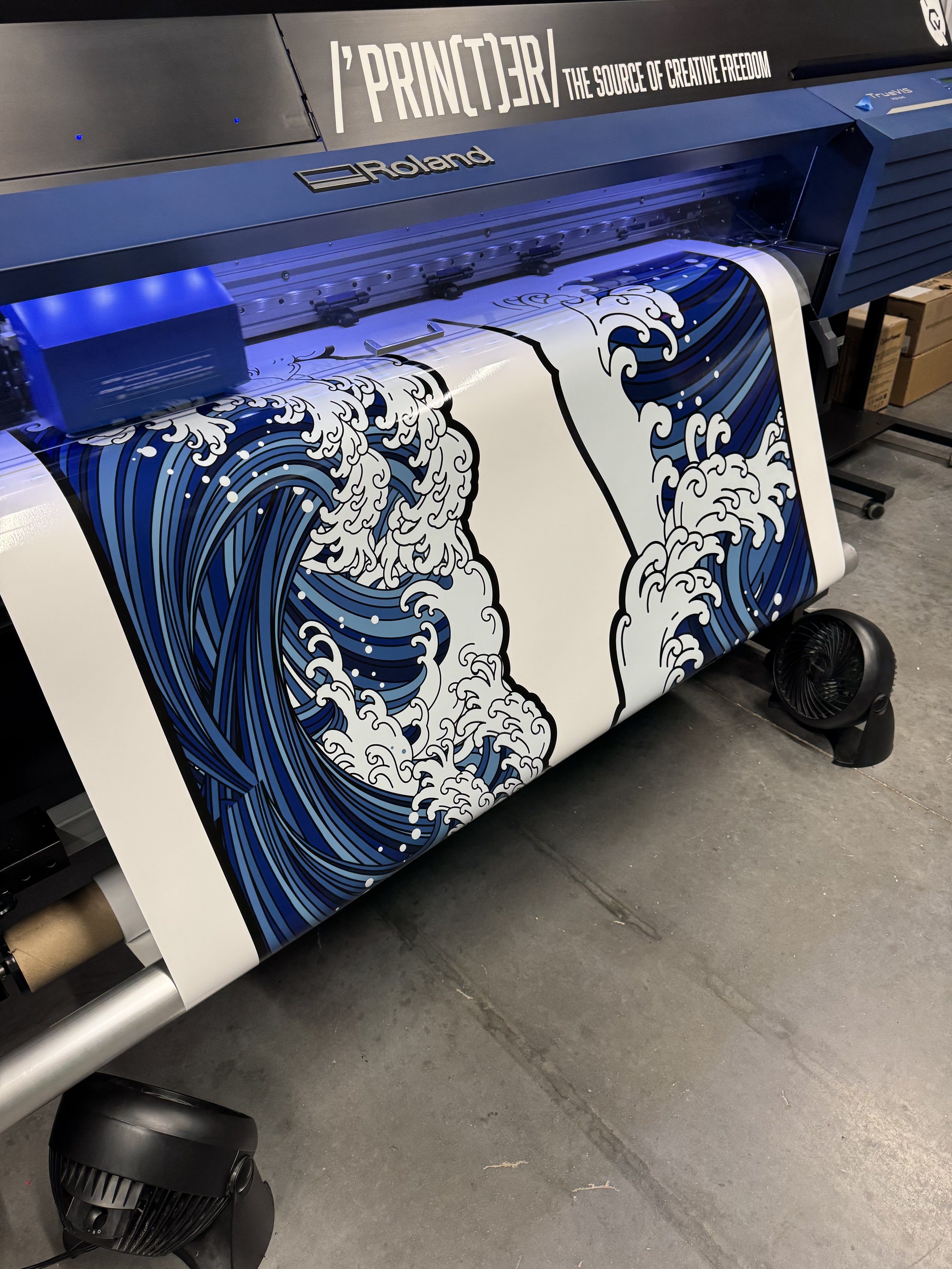 A Roland large format printer producing a print of Hokusai's Great Wave off Kanagawa on a wide sheet of material.
