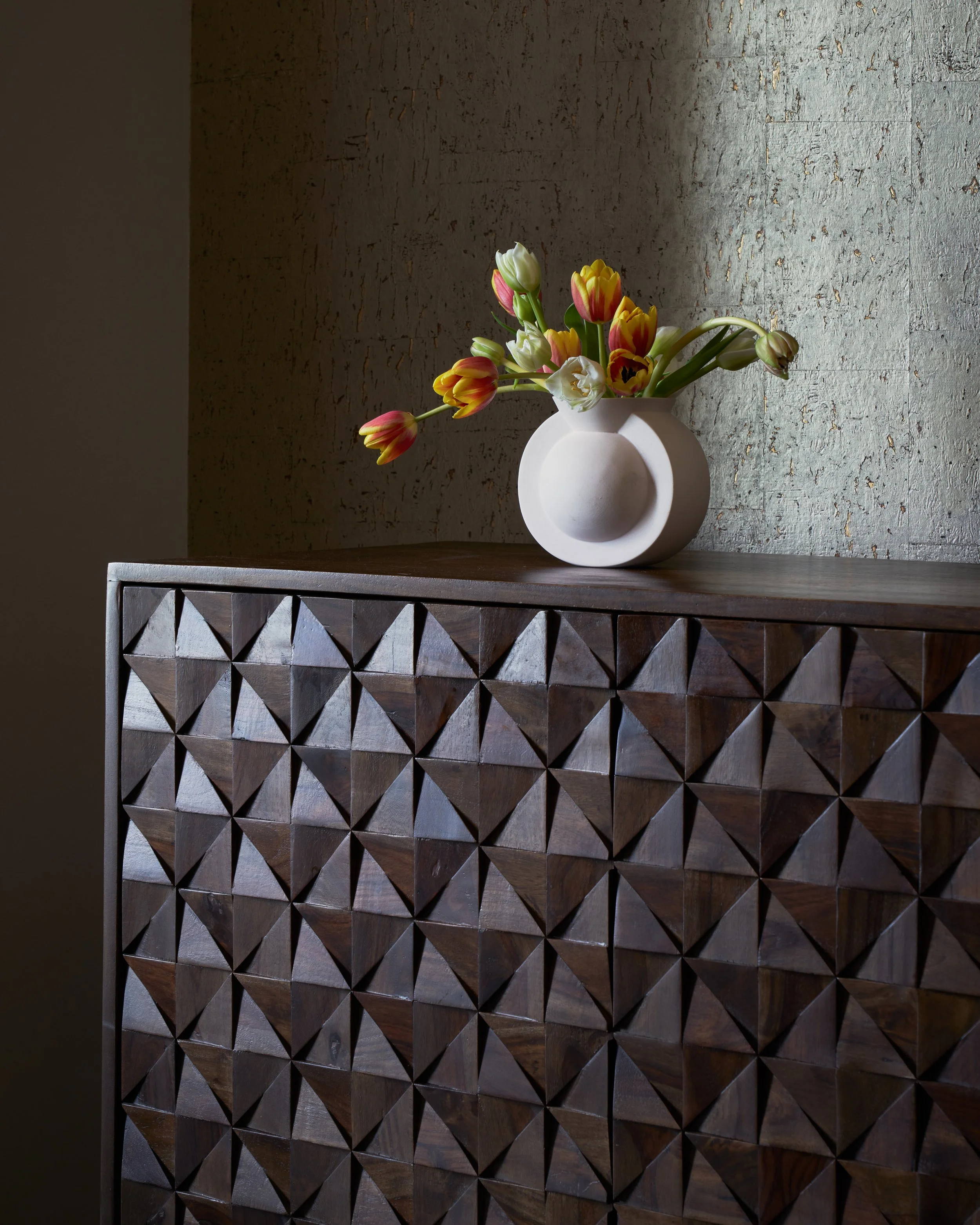 A circular white vase sits atop a sculptural geometric sideboard.