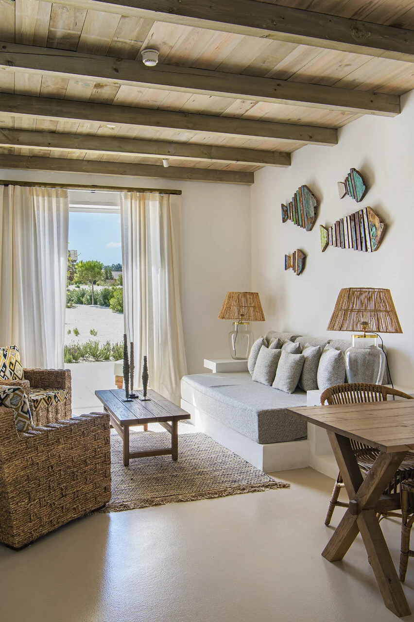 A townhouse living room with beamed ceiling and pale floor, a built-in daybed under painted fish, wicker chairs and a full-height window to the garden.