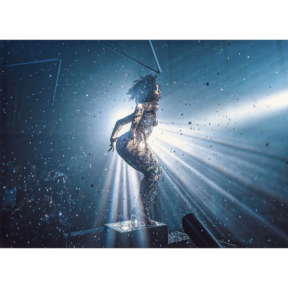 A performer in a shiny outfit dancing on stage with confetti and dramatic lighting effects.