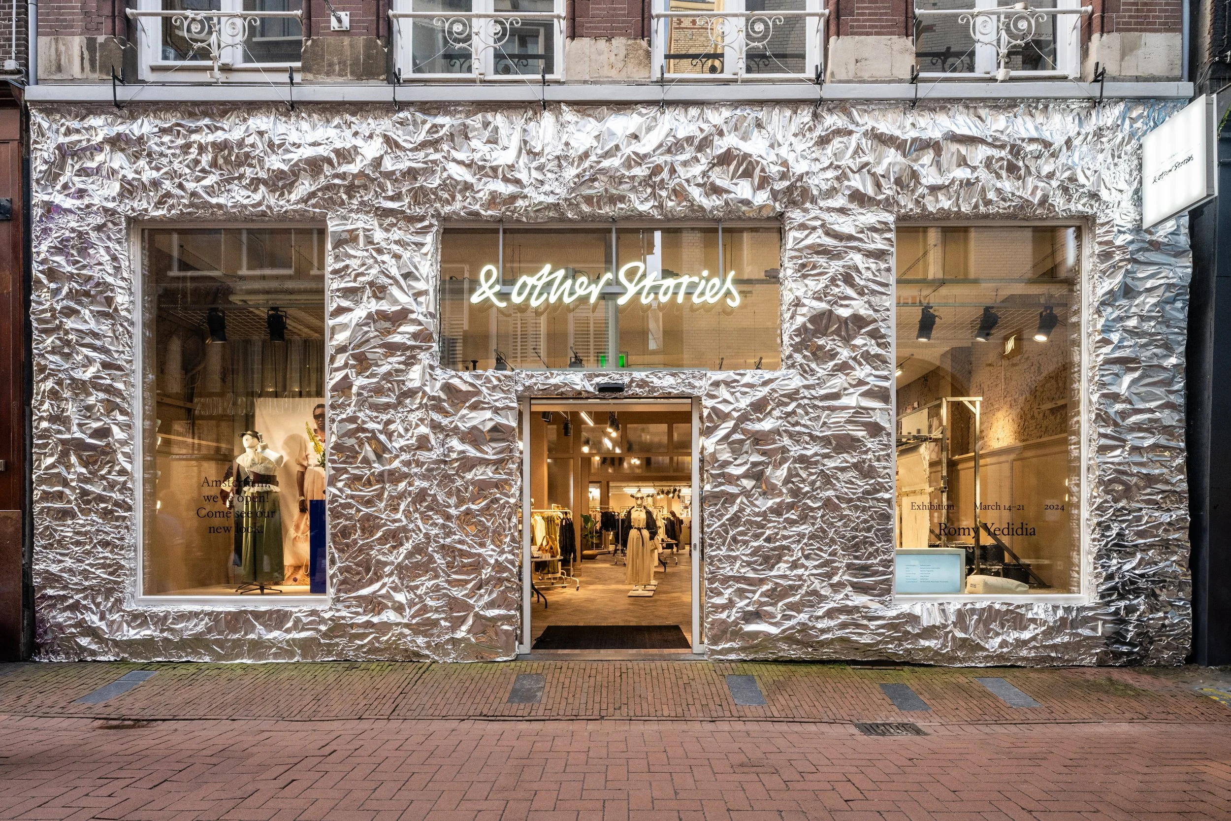 Storefront with crinkled metallic facade displaying clothing and mannequins.