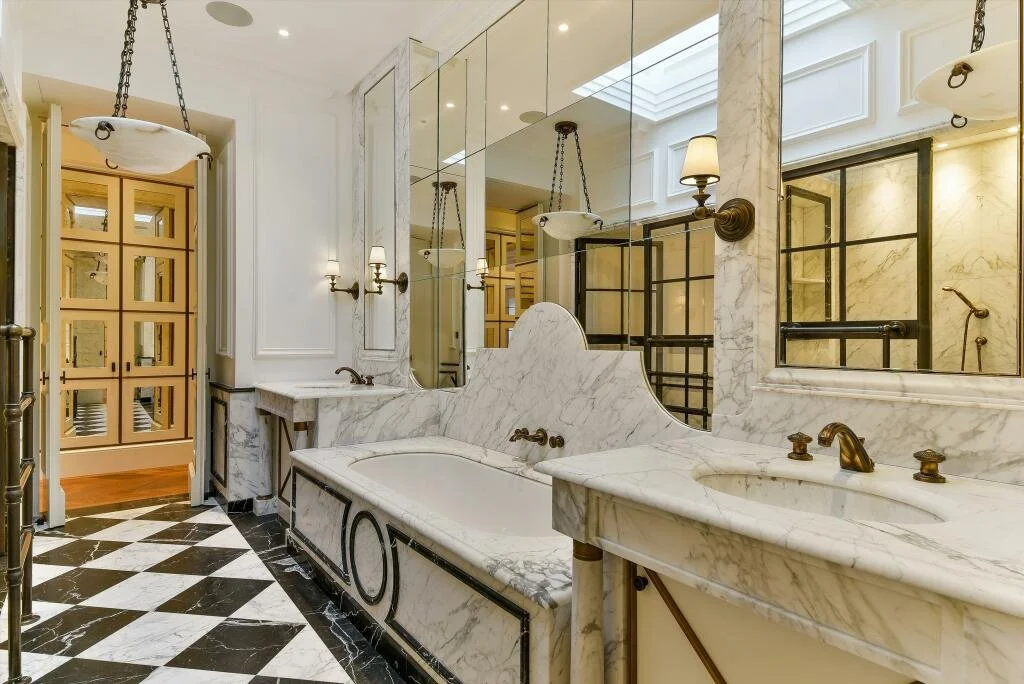 Luxury bathroom with marble finishes, large mirror, vintage-style lighting, bathtubs, and a patterned black and white checkered floor. refurbishment grade II listed building basement pool