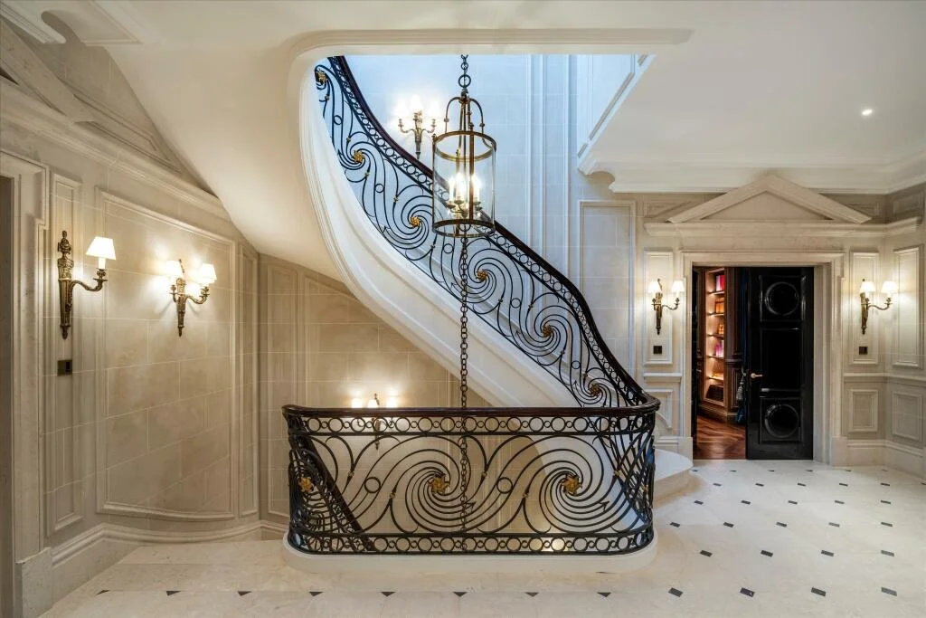Elegant staircase with ornate wrought iron banister, chandelier, and classic wall sconces in a luxurious hallway. refurbishment grade II listed building basement pool