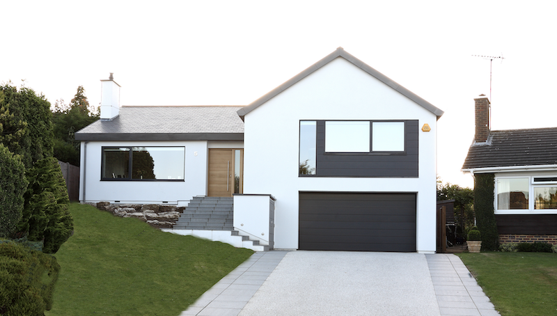 Modern two-story white render house with black accents and a grey garage door, set on a landscaped lawn with a permeable driveway and stone steps leading to the front door.