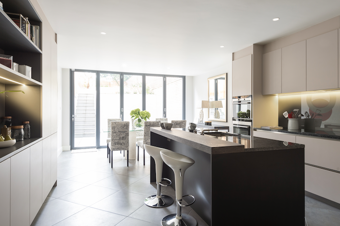 Modern kitchen with modern cabinetry, black island counter, stainless steel appliances, and large glass sliding doors leading to an outdoor area Interior design Wimbledon terraced houses basement art lighting