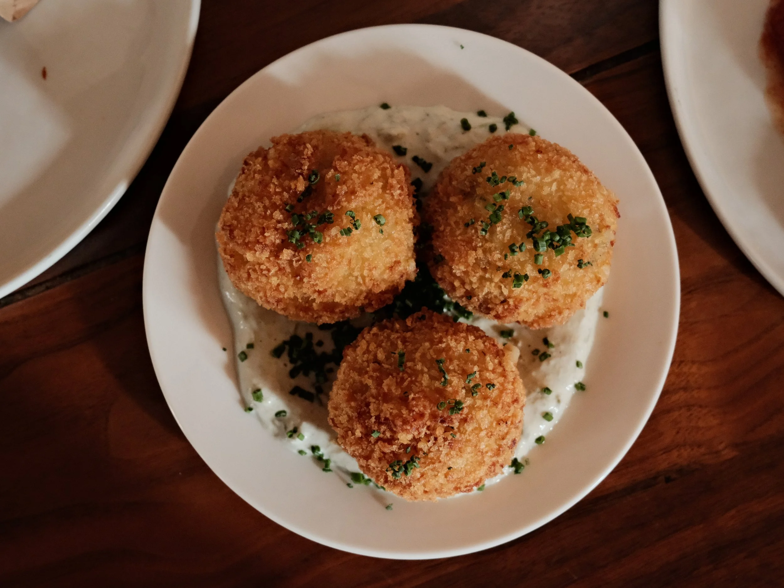 Plate with three fried croquettes garnished with chopped herbs, served on a creamy white sauce.
