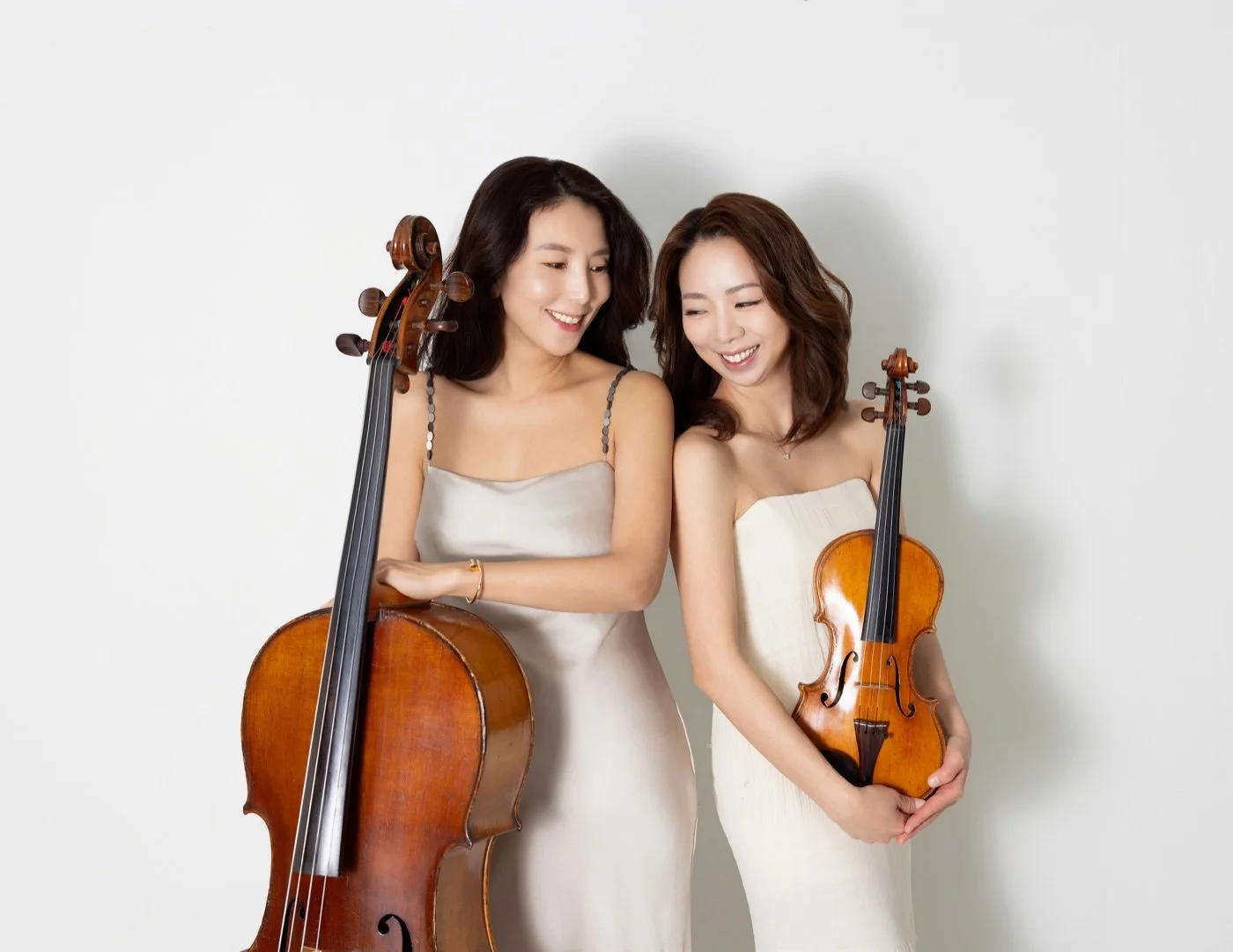 SoundNJoy violinist and cellist smiling together while holding their instruments against a light background