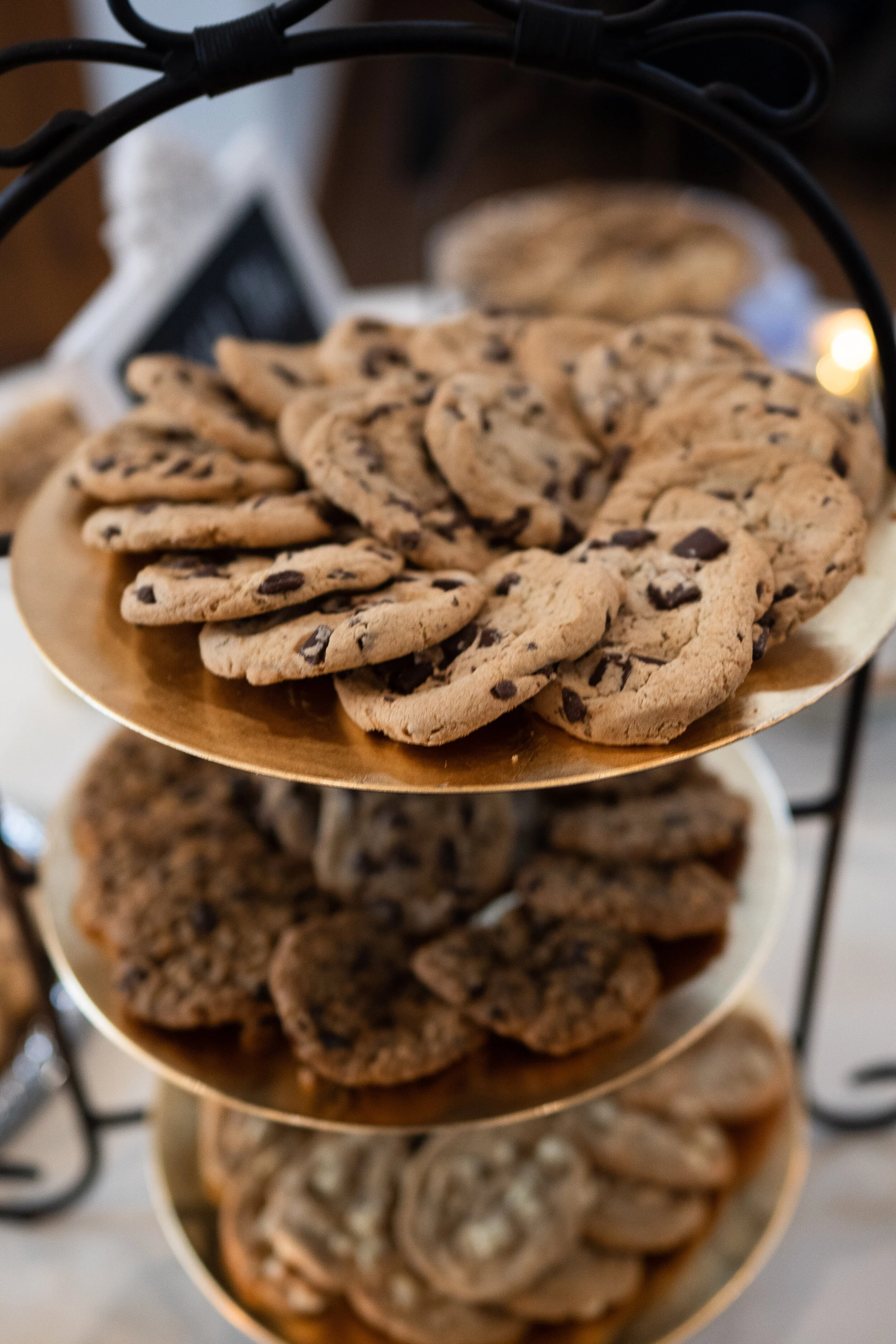 Three-tiered tray with assorted cookies, including chocolate chip, displayed on gold plates.