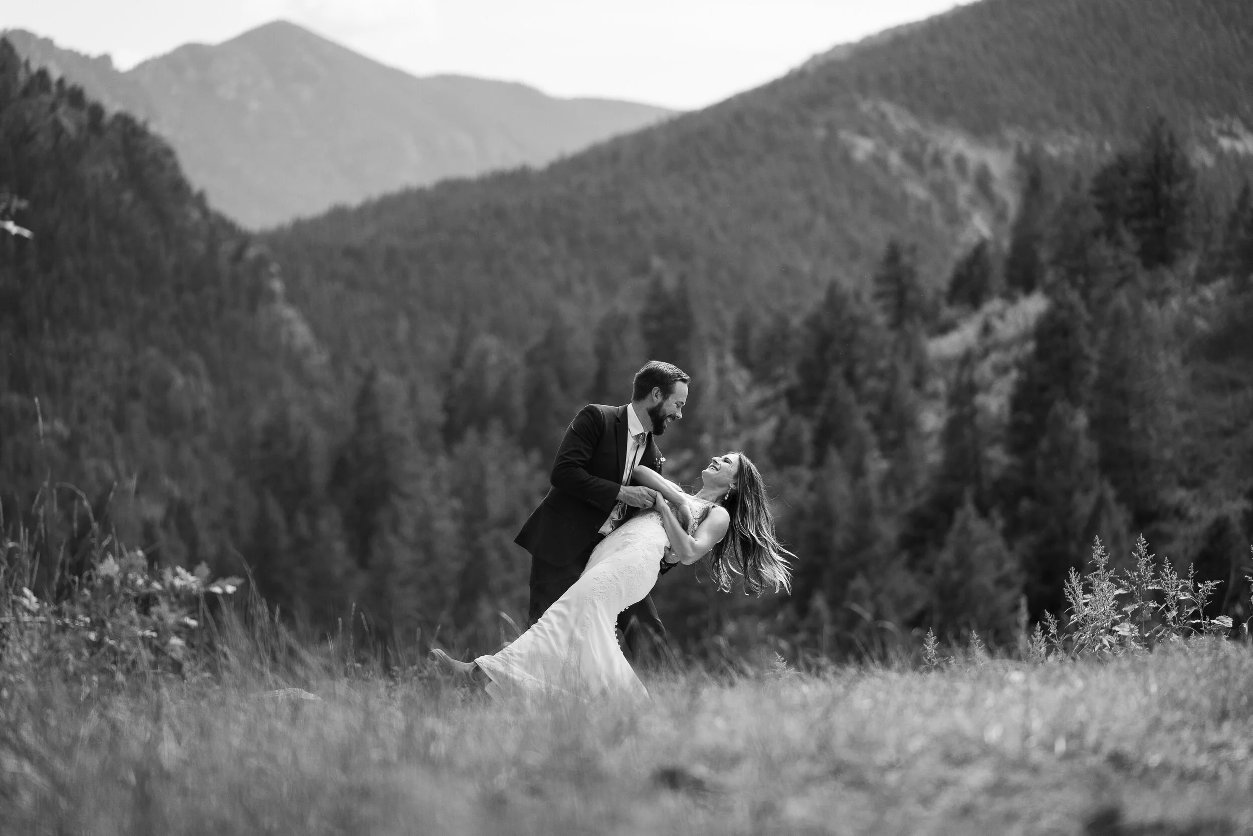 Black and white photo of a couple dancing in a grassy field with Colorado Rocky mountains in the background.
