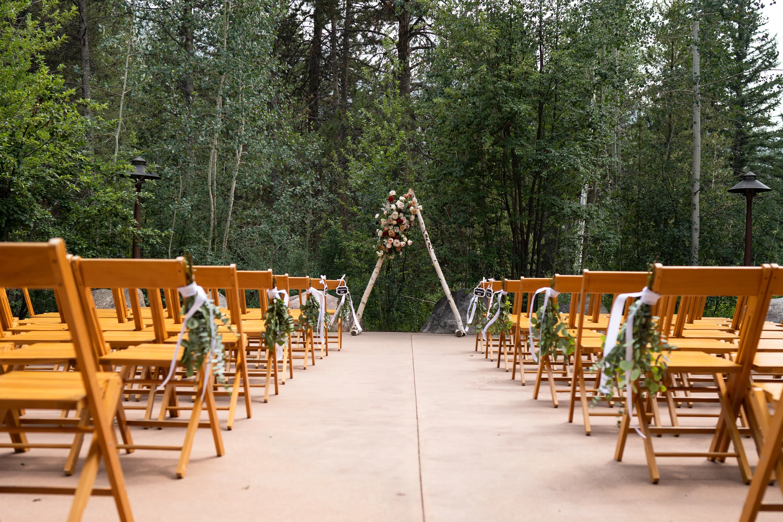 Outdoor wedding ceremony setup with wooden chairs and floral arch