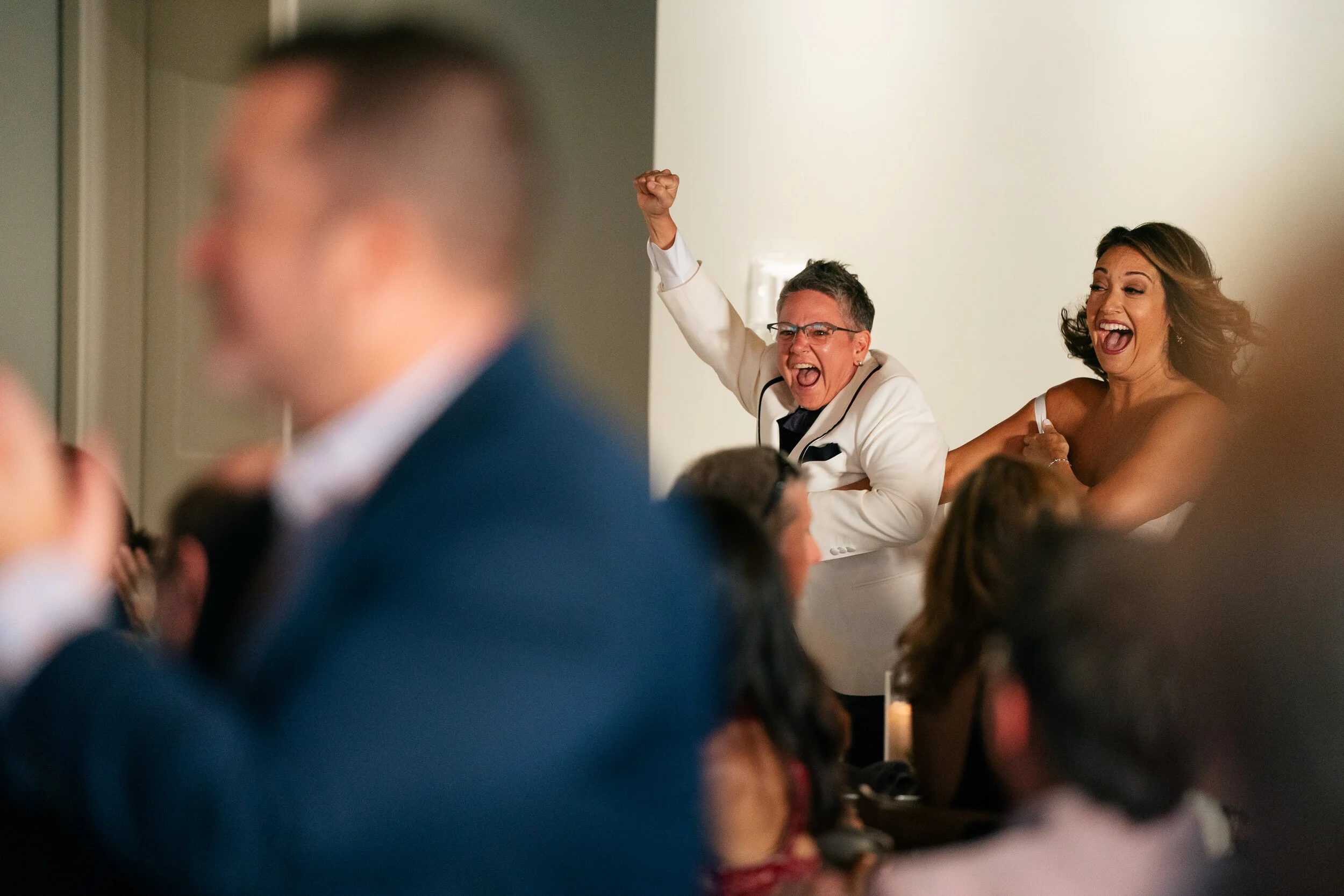 People celebrating at an event, with one person raising a fist and another smiling, among a crowd.
