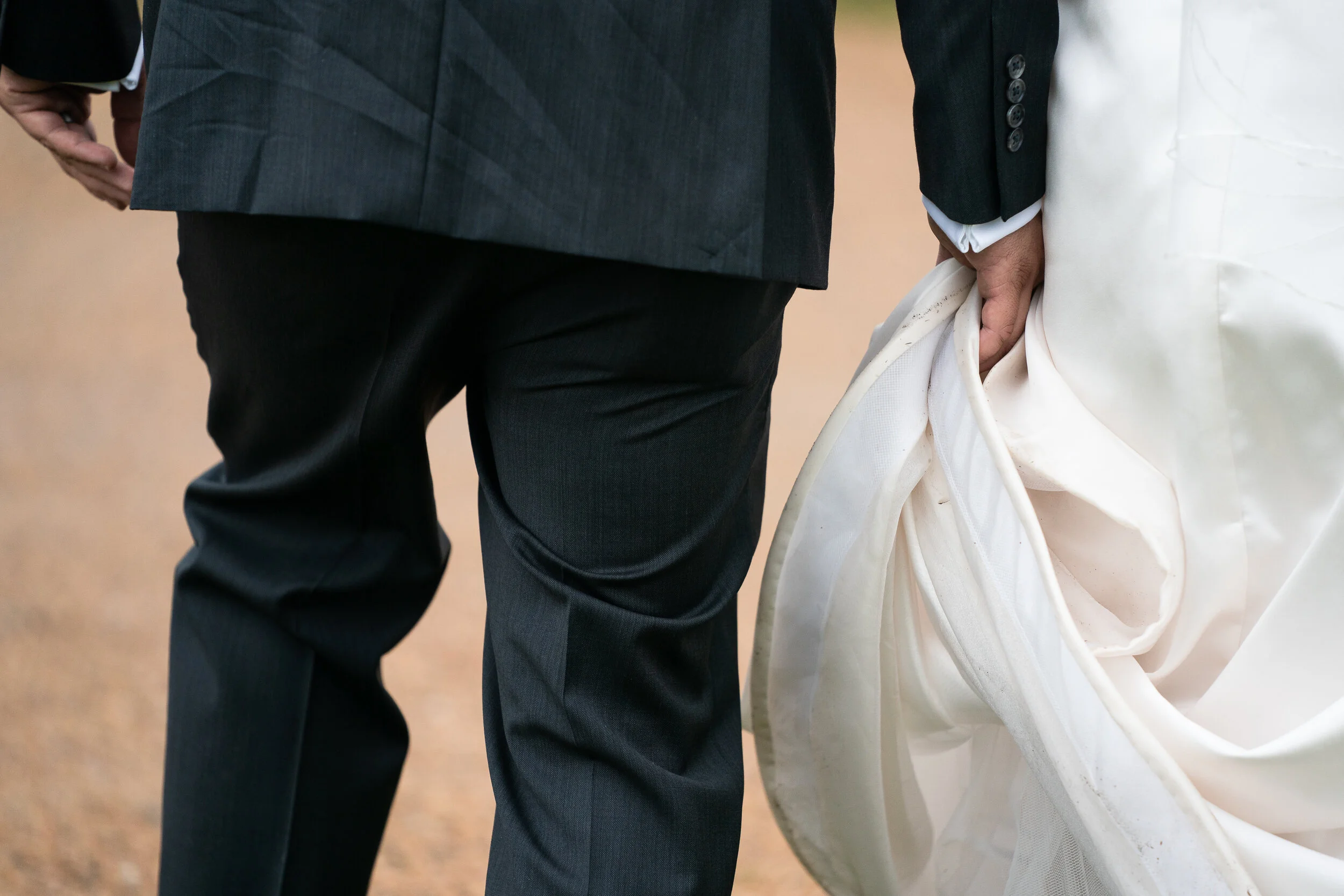 Close-up of a couple walking, with a groom in a suit and bride holding her white dress.