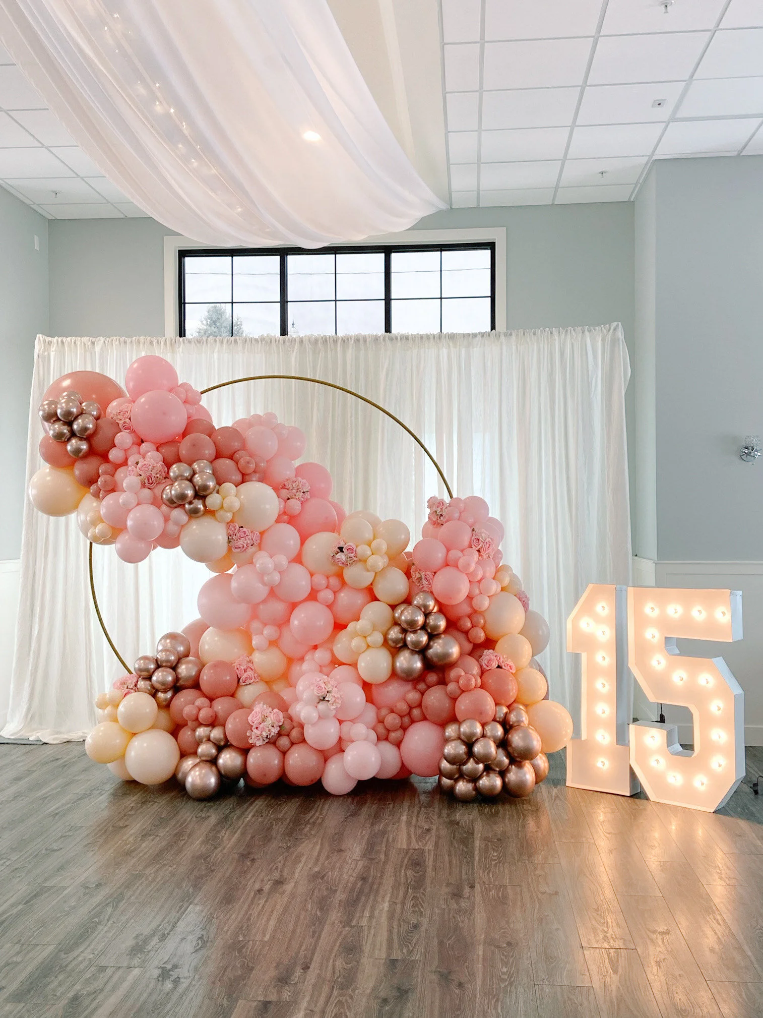 Fabulous 15th birthday bash: A dazzling, illuminated "15" marquee stands beside a stunning 7-foot gold metal circle frame adorned with a gorgeous balloon arrangement in shades of pink, rose gold, and cream. A perfect blend of elegance and celebration