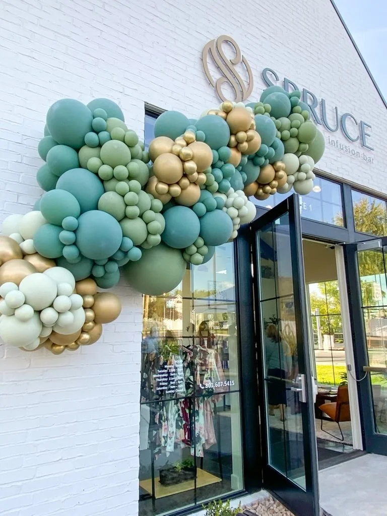 Grand opening celebration at Spruce Aesthetics featuring a vibrant balloon arch in shades of green, gold, and cream, welcoming guests with style and elegance.