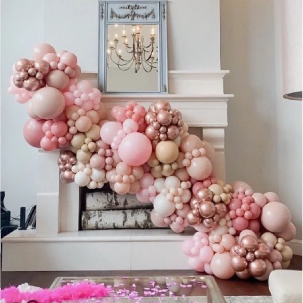 Stunning baby shower ambiance: A lavish balloon installation in pink, cream, rose gold, and tan cascades over a grand fireplace adorned with giant birch logs. Reflecting in the mantle mirror is a captivating chandelier, enhancing the enchanting atmos