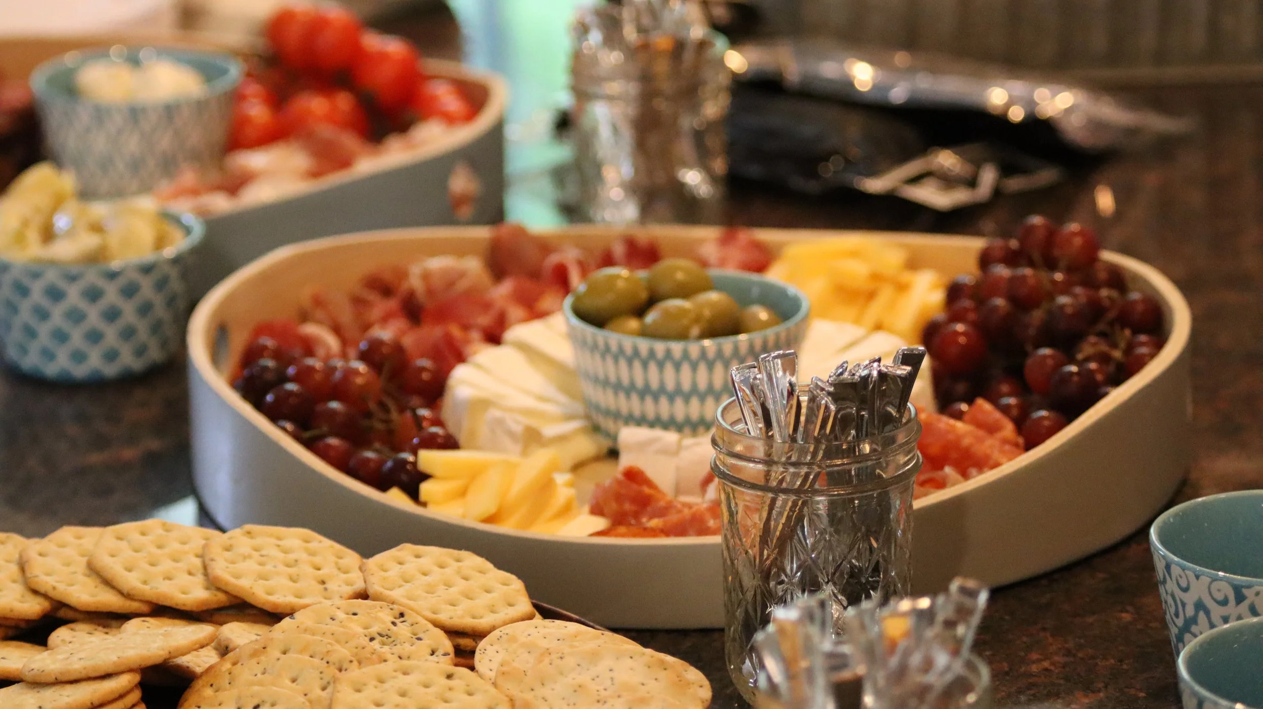 A cheese and grape platter with crackers, small bowls of cheese and grapes, and small dessert cups on a table.