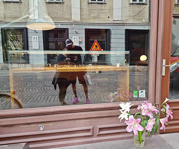 Pink lilies in front of a jewelry store. A tall man and short woman lean into each other in the window reflection.
