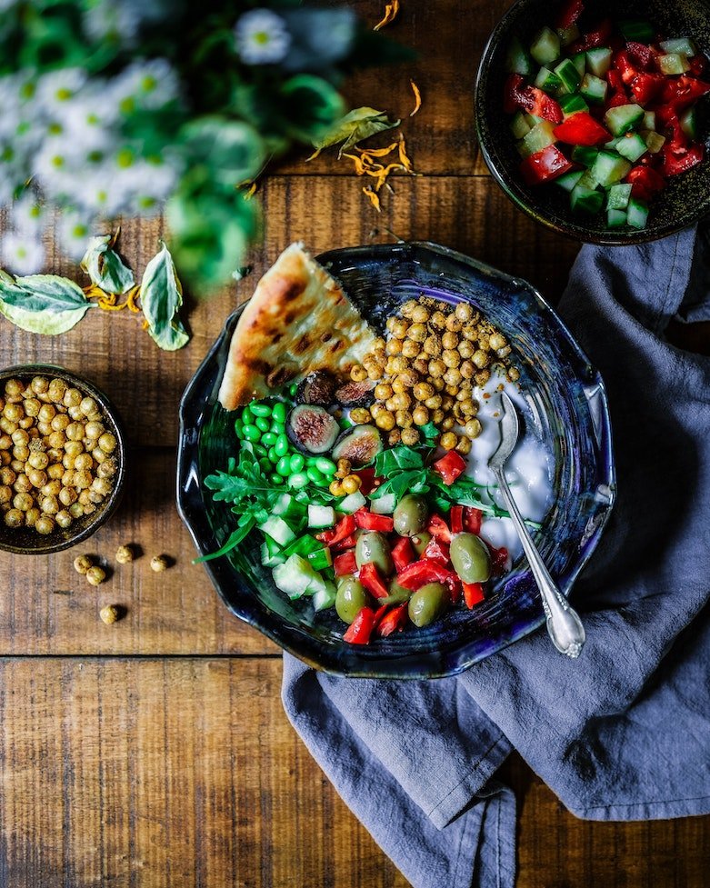 Salatschüssel mit Kichererbsen, Oliven, Paprika, Erbsen und Brot auf Holztisch.
