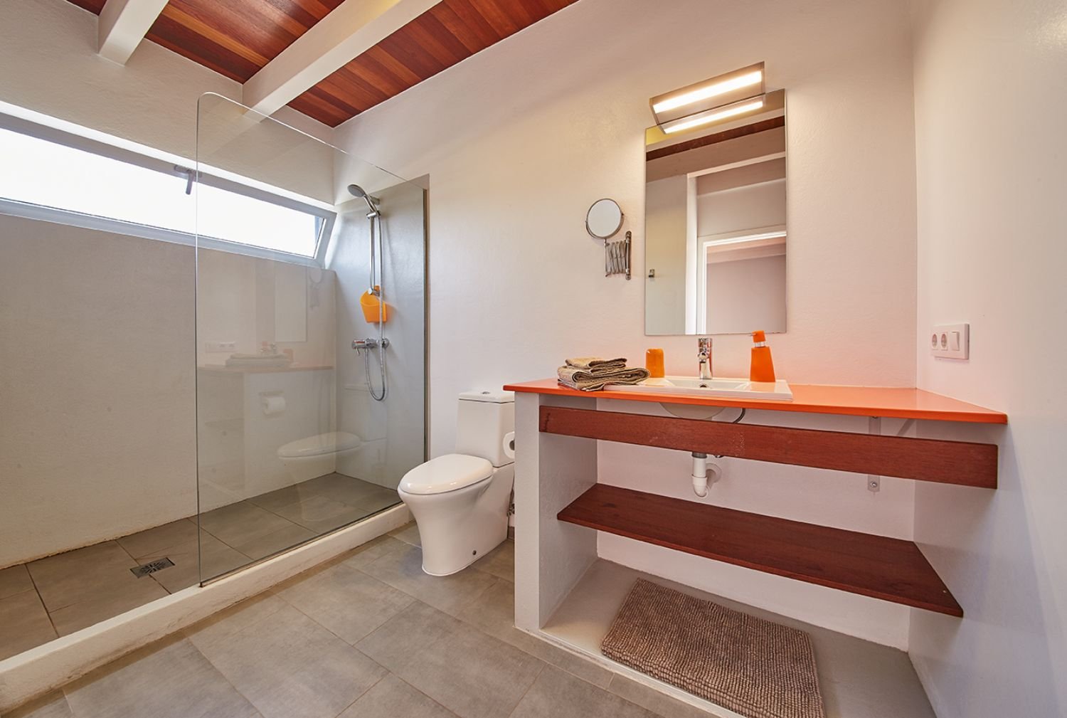 Modernes Badezimmer mit begehbarer Dusche, WC und Waschbecken mit orangefarbener Arbeitsplatte und Spiegel.