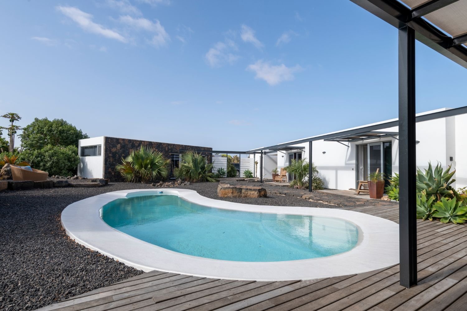Moderne Villa mit Swimmingpool, umgeben von Pflanzen und einer Terrasse. Architektur im minimalistischen Stil, klarer Himmel im Hintergrund.