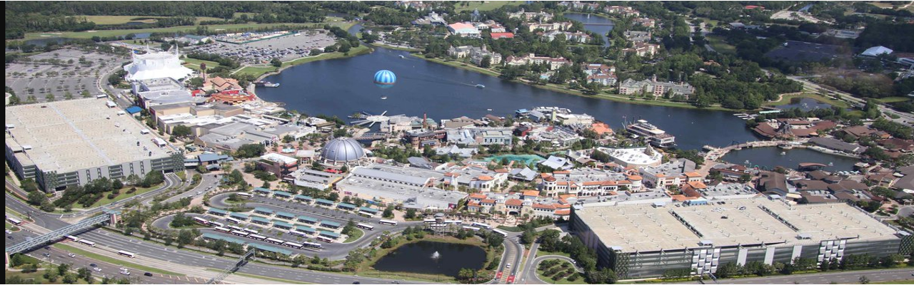 Aerial view of a large entertainment complex with a water park, parking lots, a lake with a parasail, and surrounding buildings and roads.